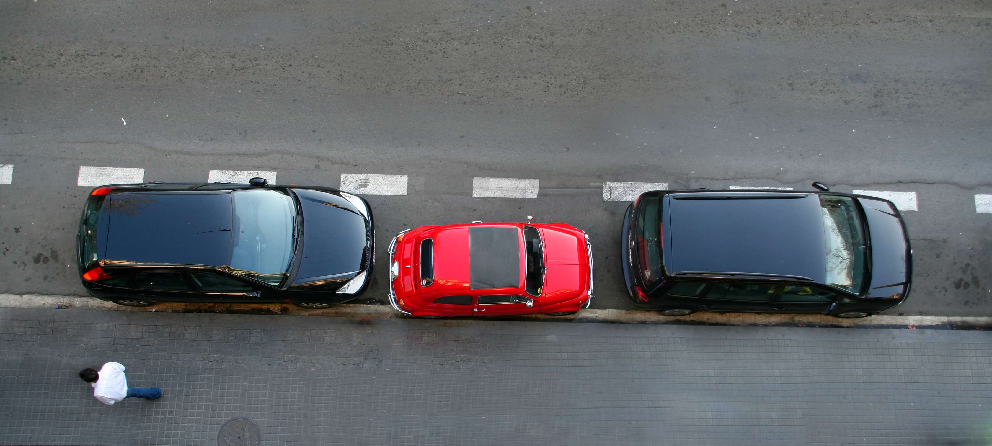 Zweitwagen versichern: Roter Kleinwagen parkt auf Straße zwischen zwei schwarzen Pkw