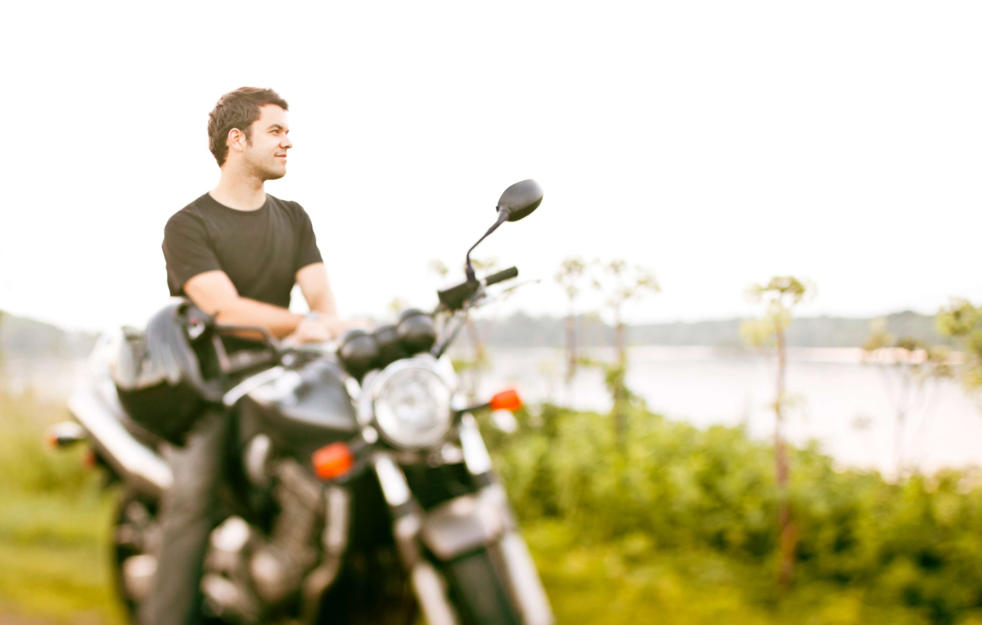 Motorrad Versicherung: Mann sitzt auf Motorrad und blickt auf See