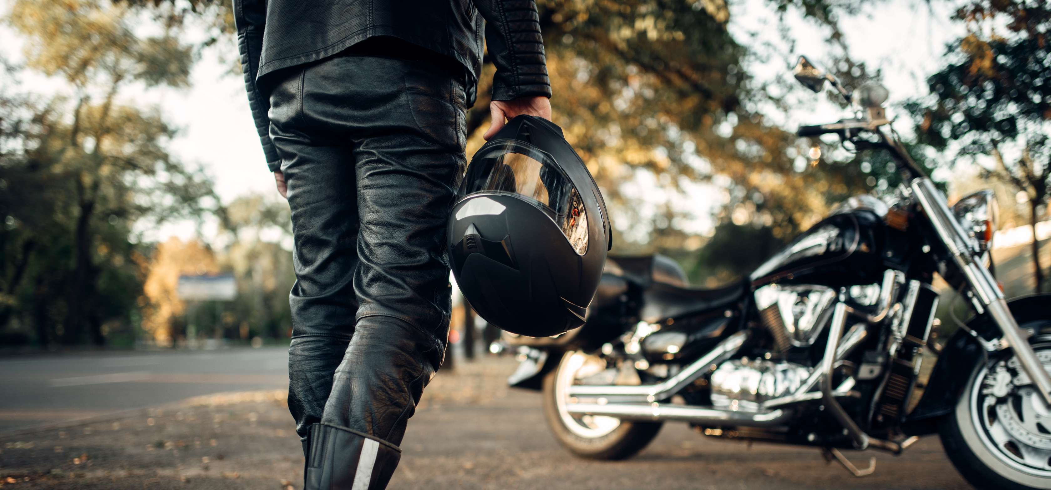 Motorrad anmelden: Mann in Lederkluft steht vor Motorrad und hält Helm in rechter Hand