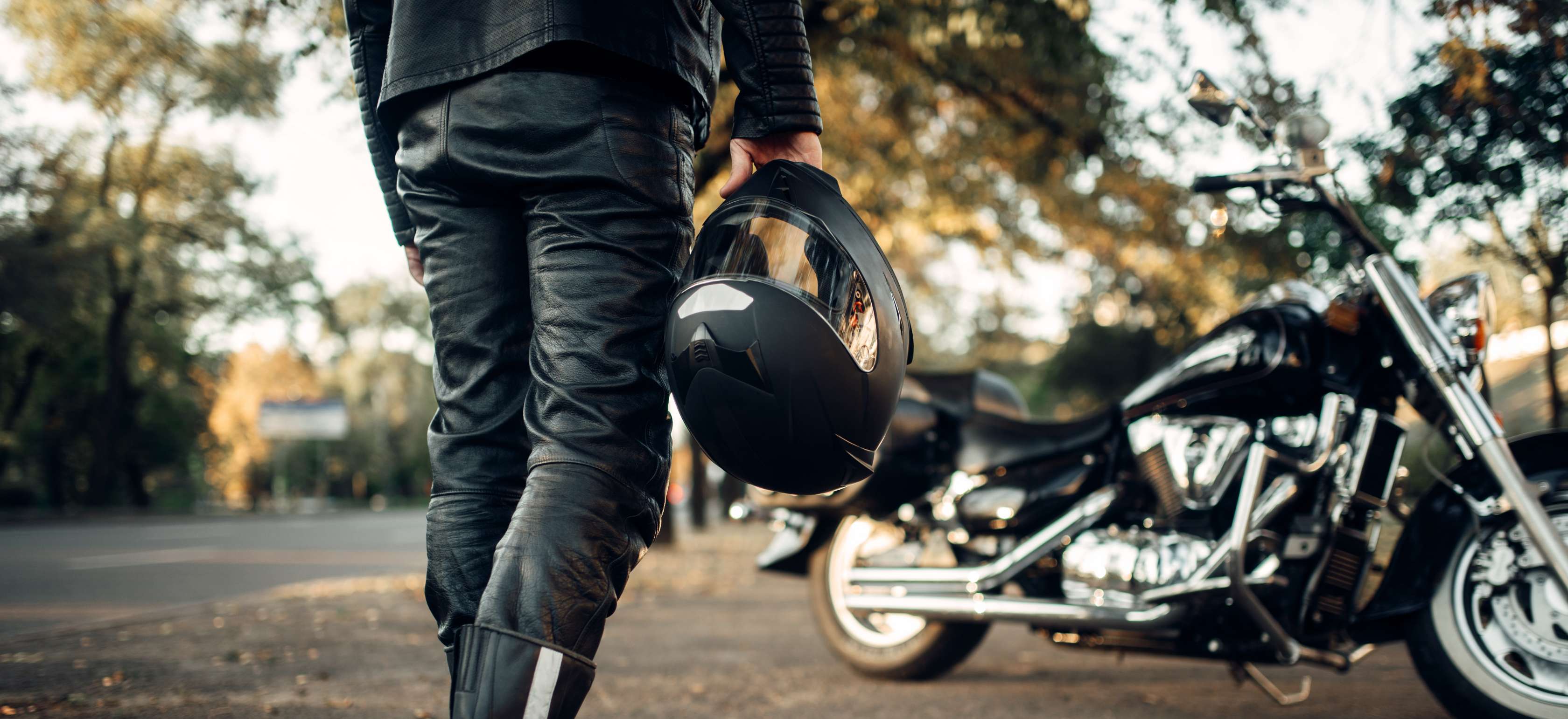 Motorrad anmelden: Mann in Lederkluft steht vor Motorrad und hält Helm in rechter Hand