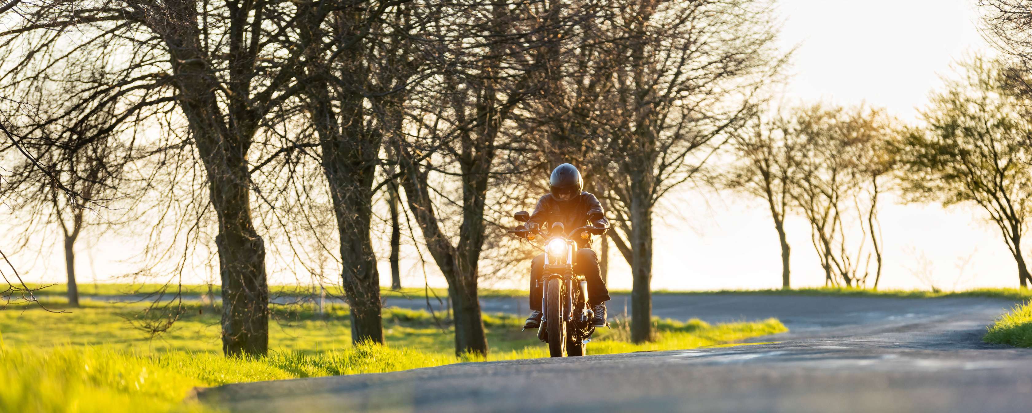 Motorrad Versicherungsklassen: Motorradfahrer mit Helm und schwarzer Schutzkleidung fährt auf Landstraße