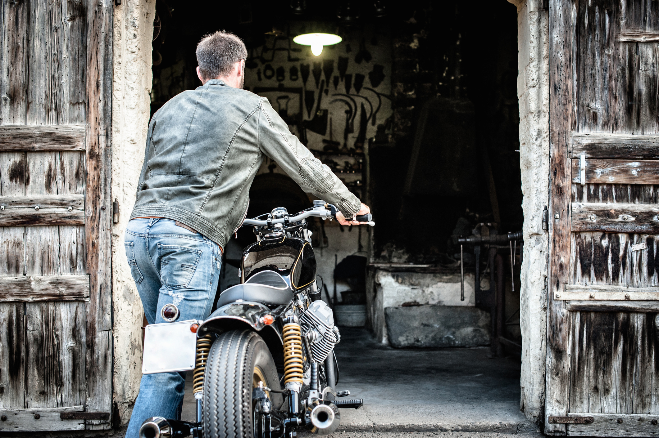 Allianz - Saisonkennzeichen Motorrad: Mann mit Jeans und Lederjacke schiebt Motorrad in eine Garage