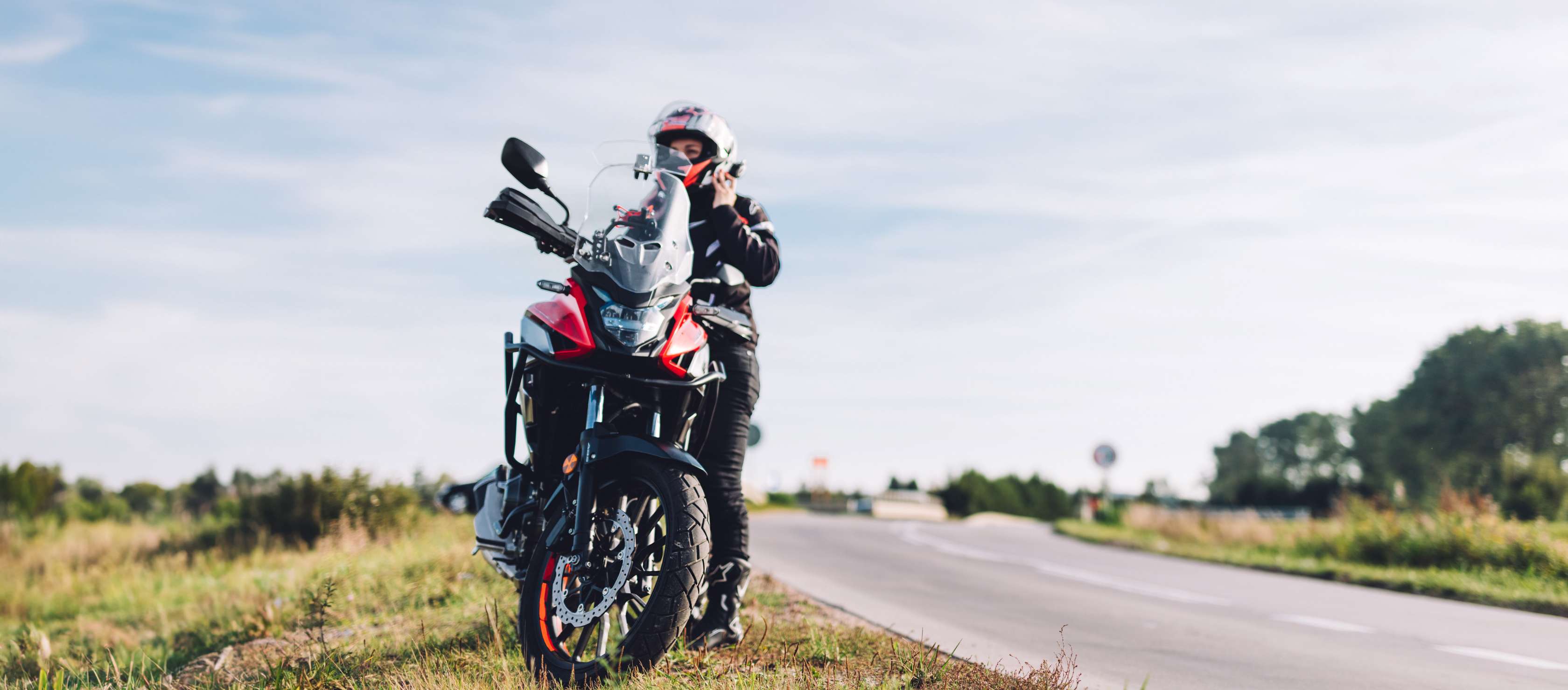 Motorrad Schutzbrief: Frau stellt Motorrad auf Grünfläche neben Landstraße ab