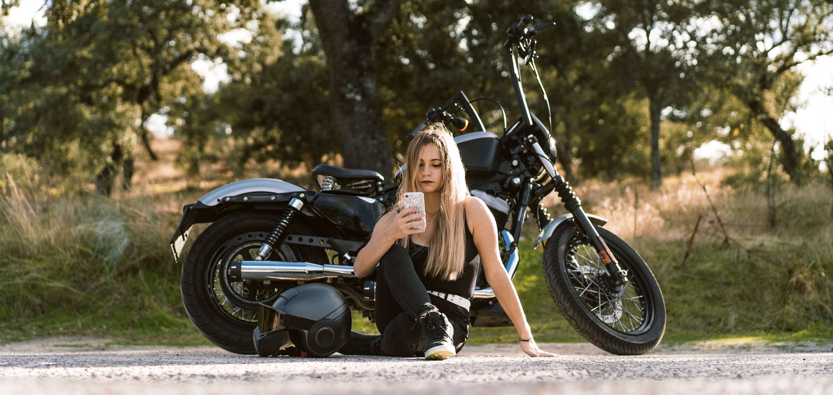 Motorrad Vollkasko: Junge Frau sitzt vor ihrem Motorrad und blickt auf ihr Smartphone