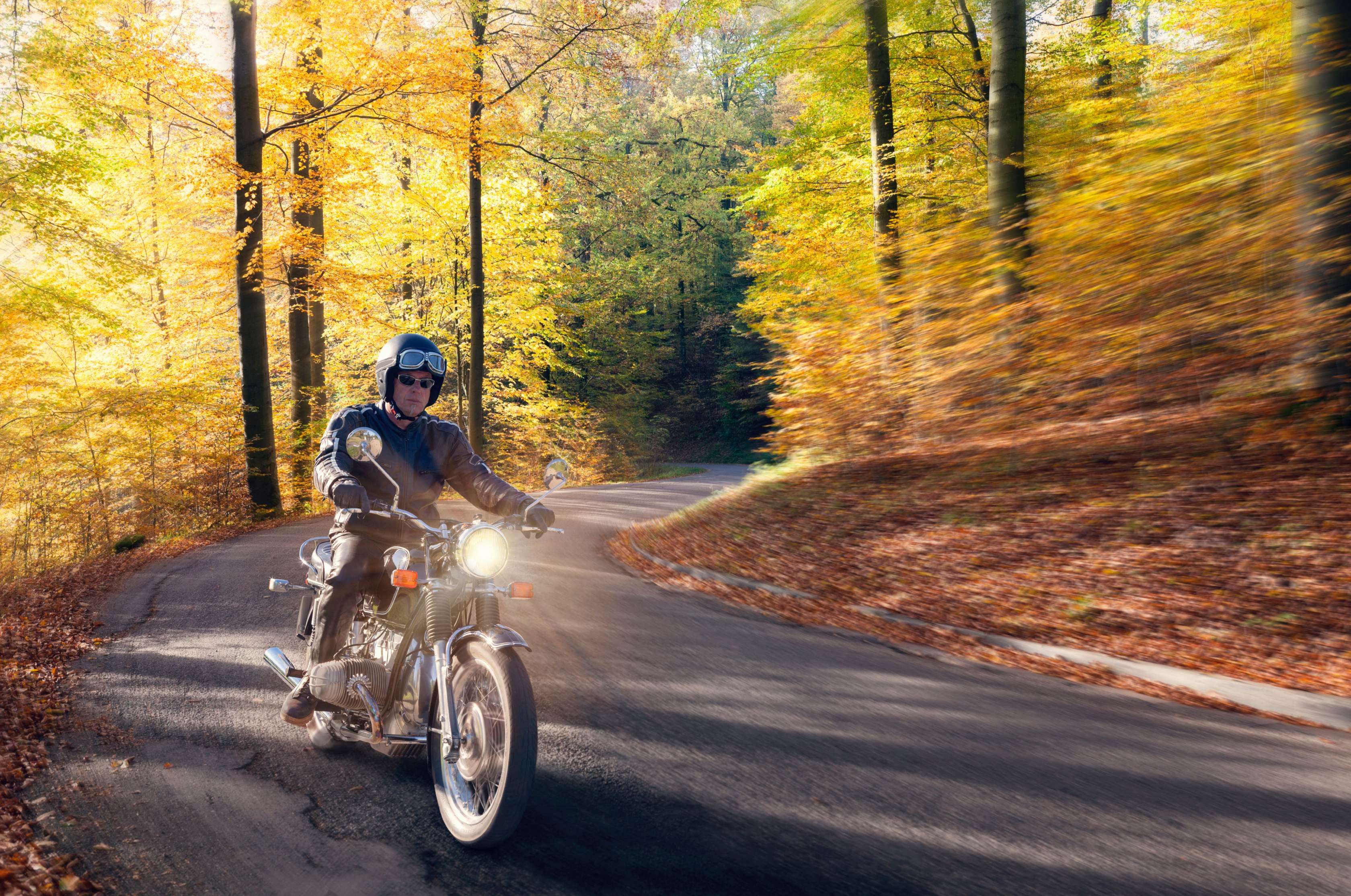 Mann fährt mit Oldtimer-Motorrad auf einer Strasse durch einen Wald