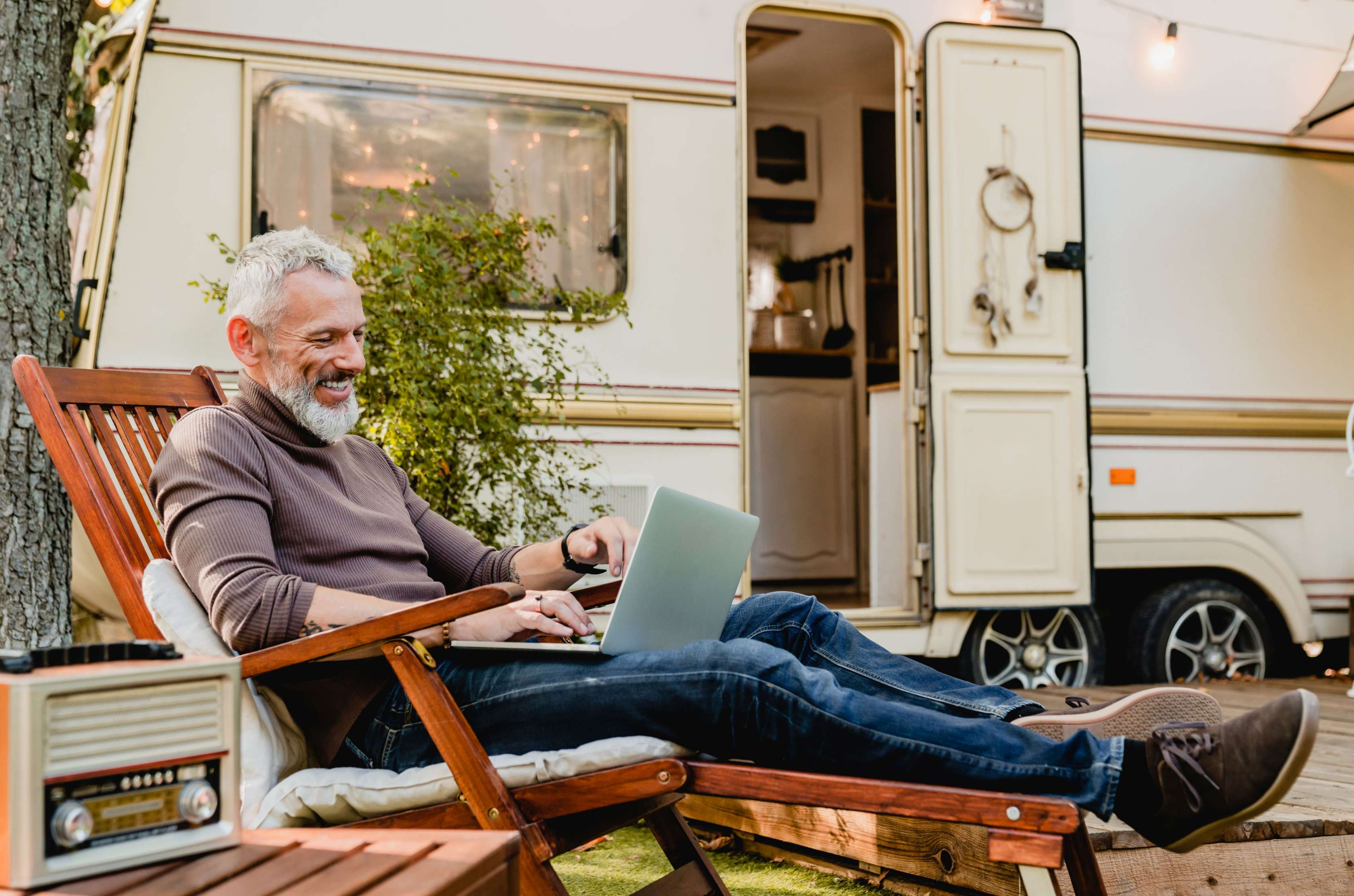 Mann sitzt mit Laptop im Liegestuhl vor seinem Wohnmobil mit H-Kennzeichen