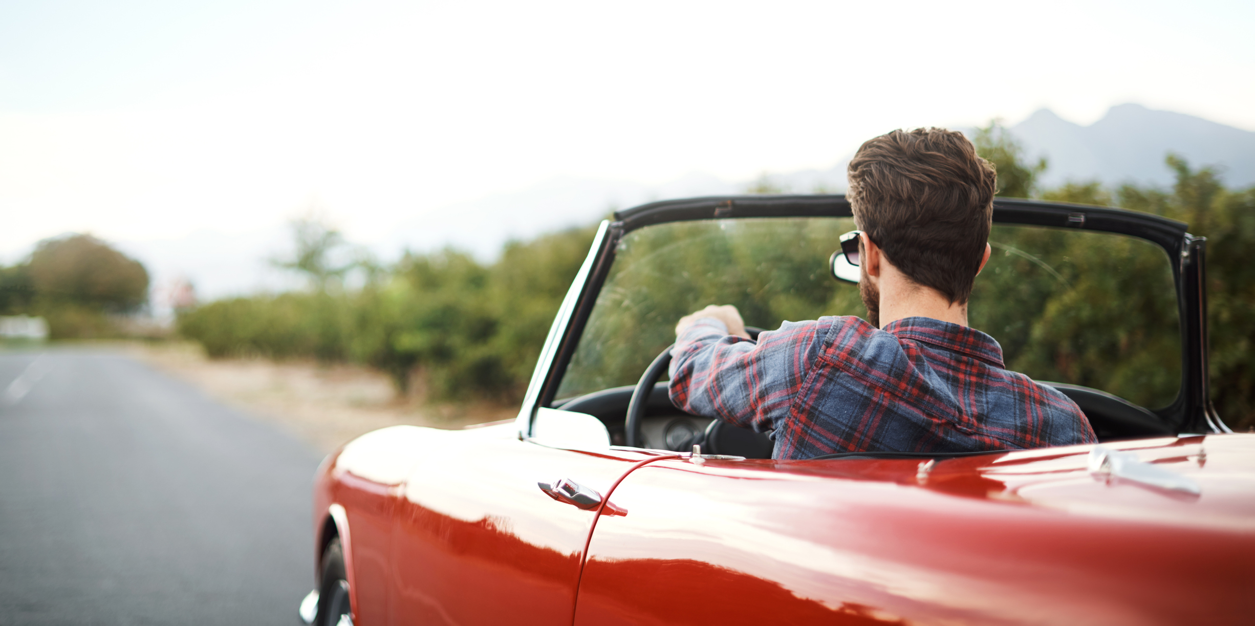 Junger Mann fährt in einem roten Oldtimer-Cabrio eine Landstraße entlang
