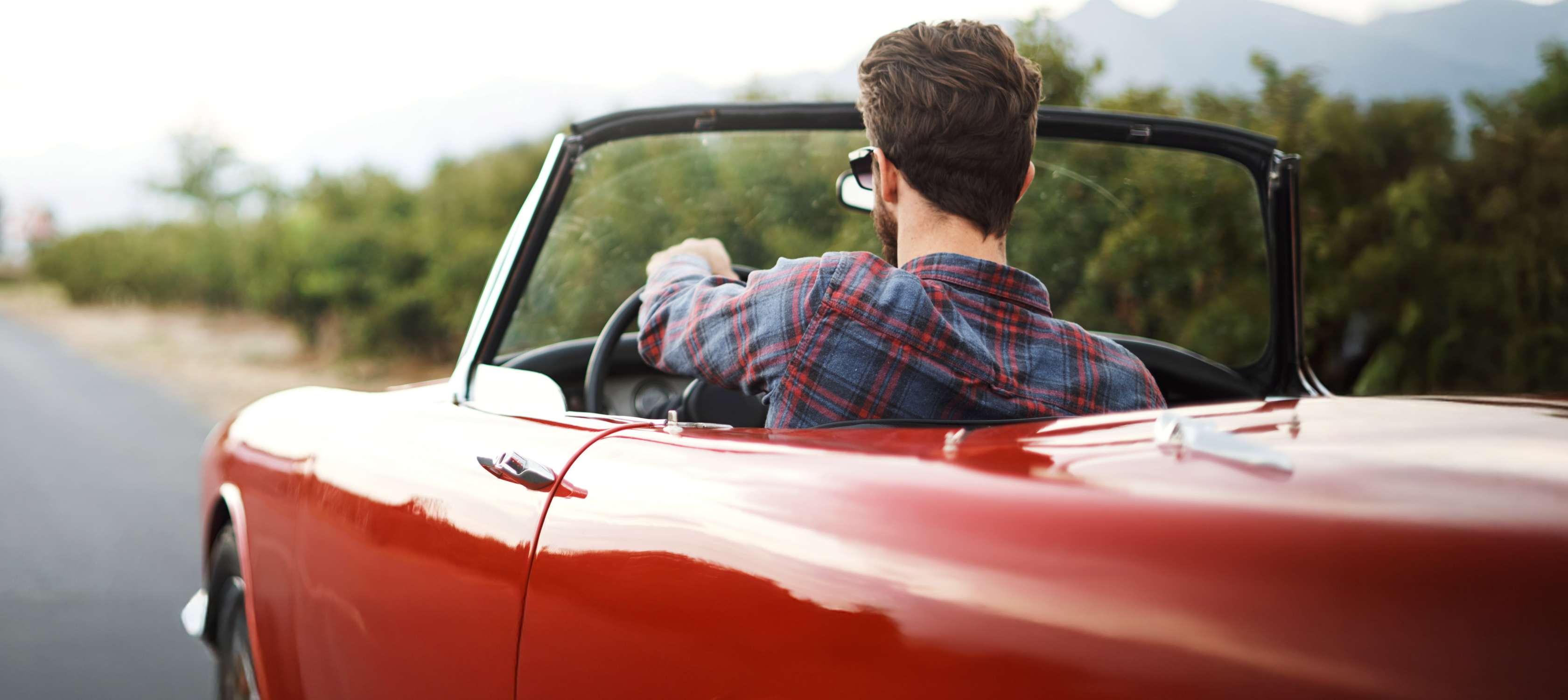 Oldtimer Zulassung: Mann fährt in rotem Oldtimer-Cabrio auf Landstraße