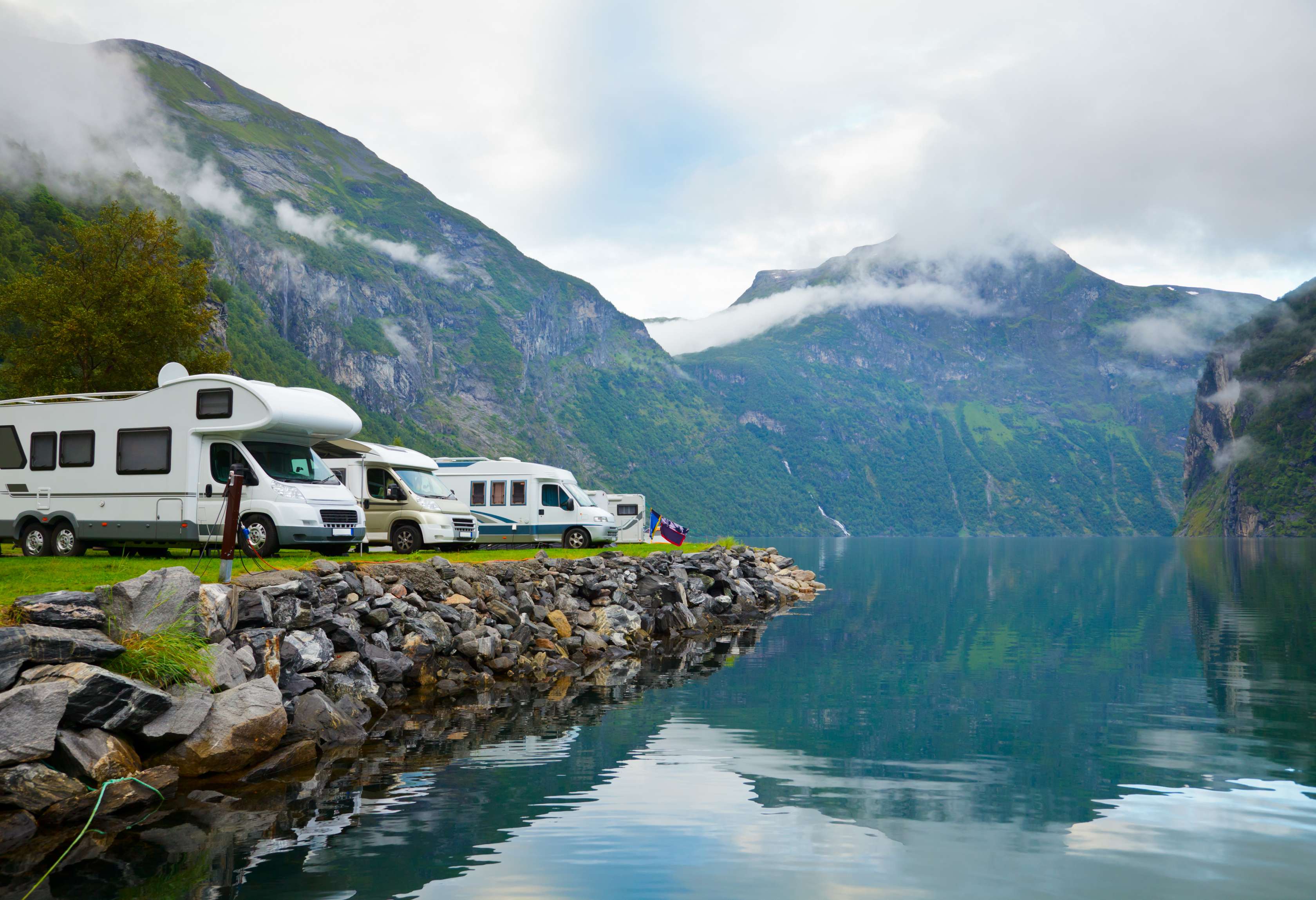 Wohnmobile stehen auf einem Campingplatz direkt am Ufer eines Bergsees