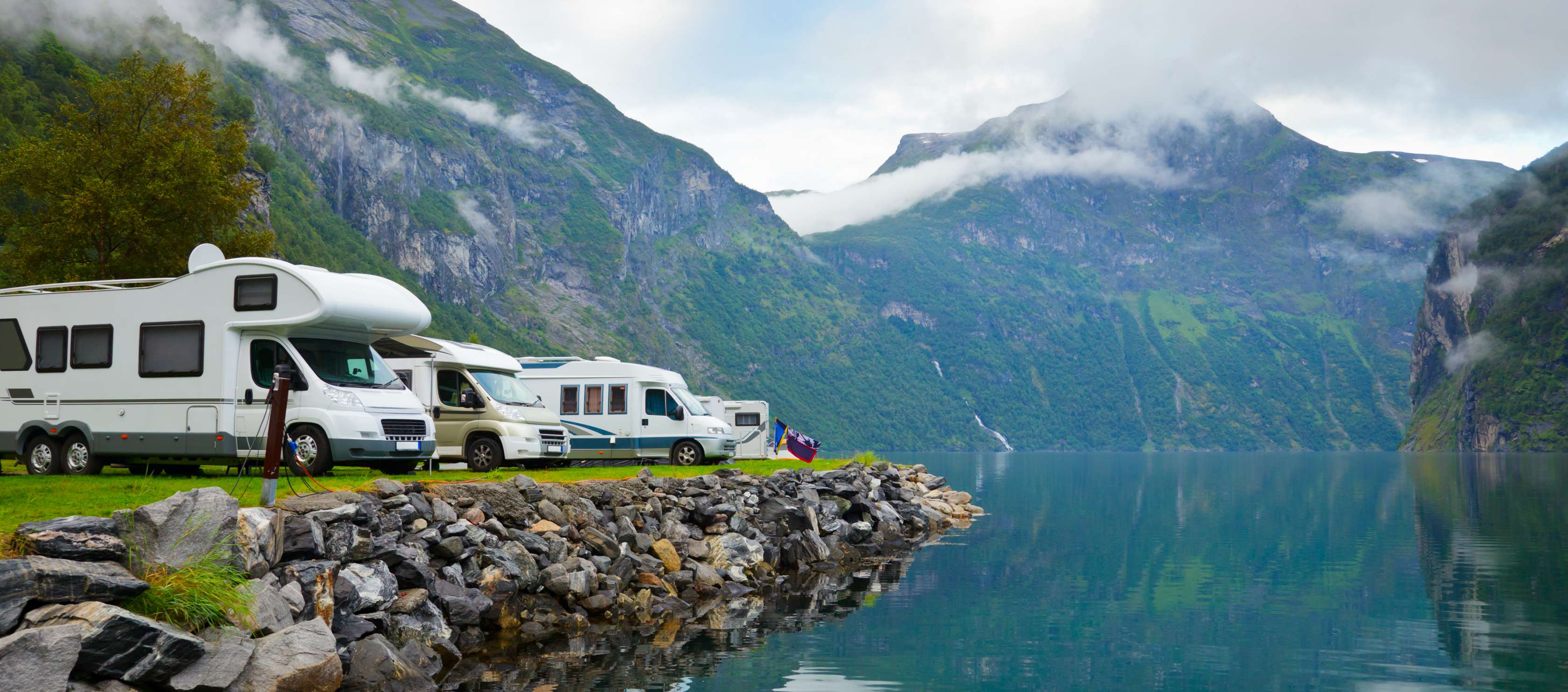 Allianz - Wohnmobil Versicherung: Mehrere Campingfahrzeuge stehen an Ufer eines Bergsees