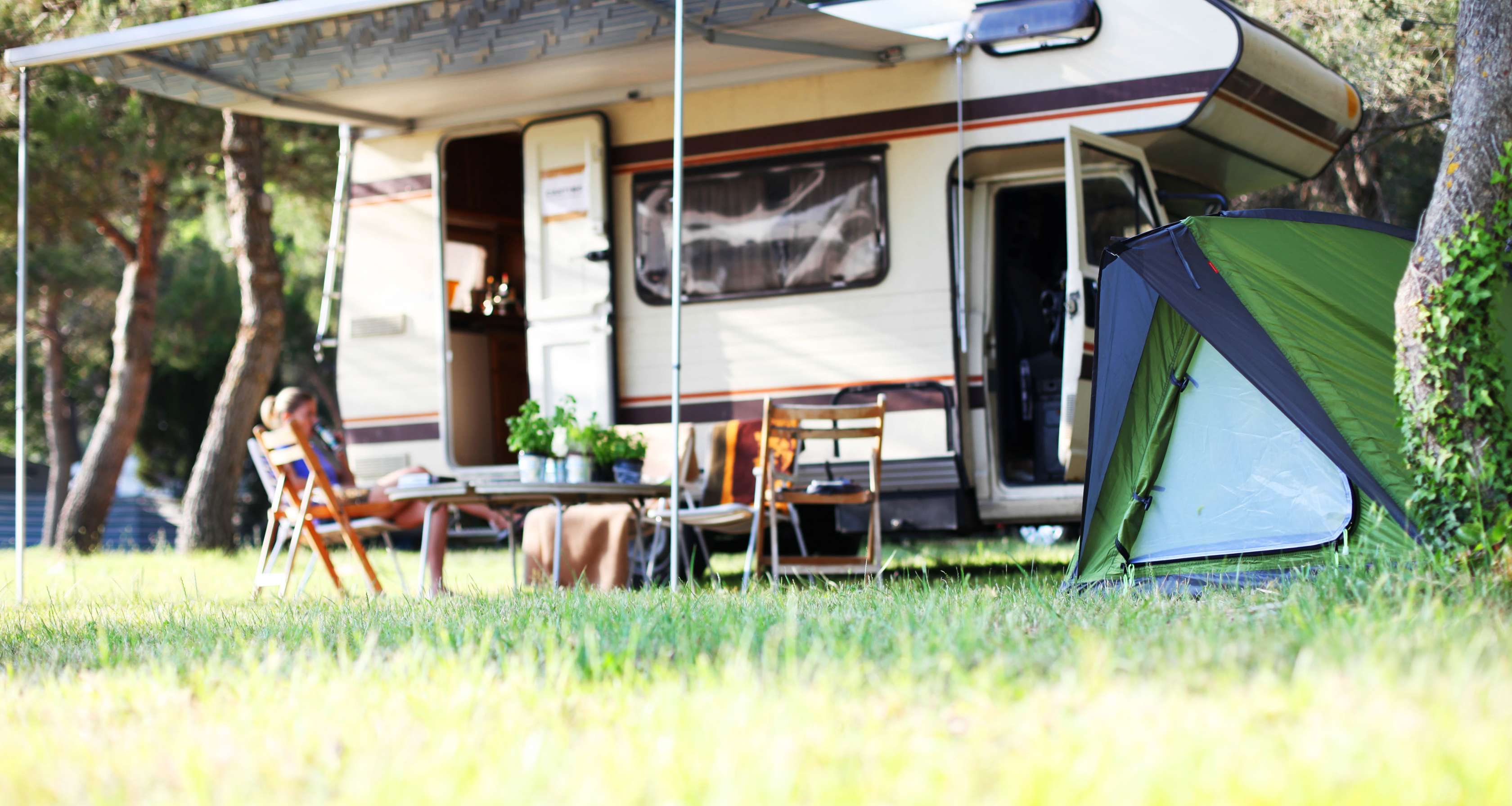 Wohnmobil mit Markise, Campingausrüstung und Zelt steht im Grünen