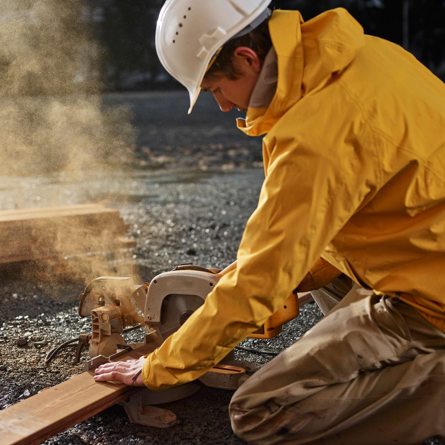 Bauleistungsversicherung - Bauarbeiter in gelber Jacke sägt Holzlatte mit Kreissäge