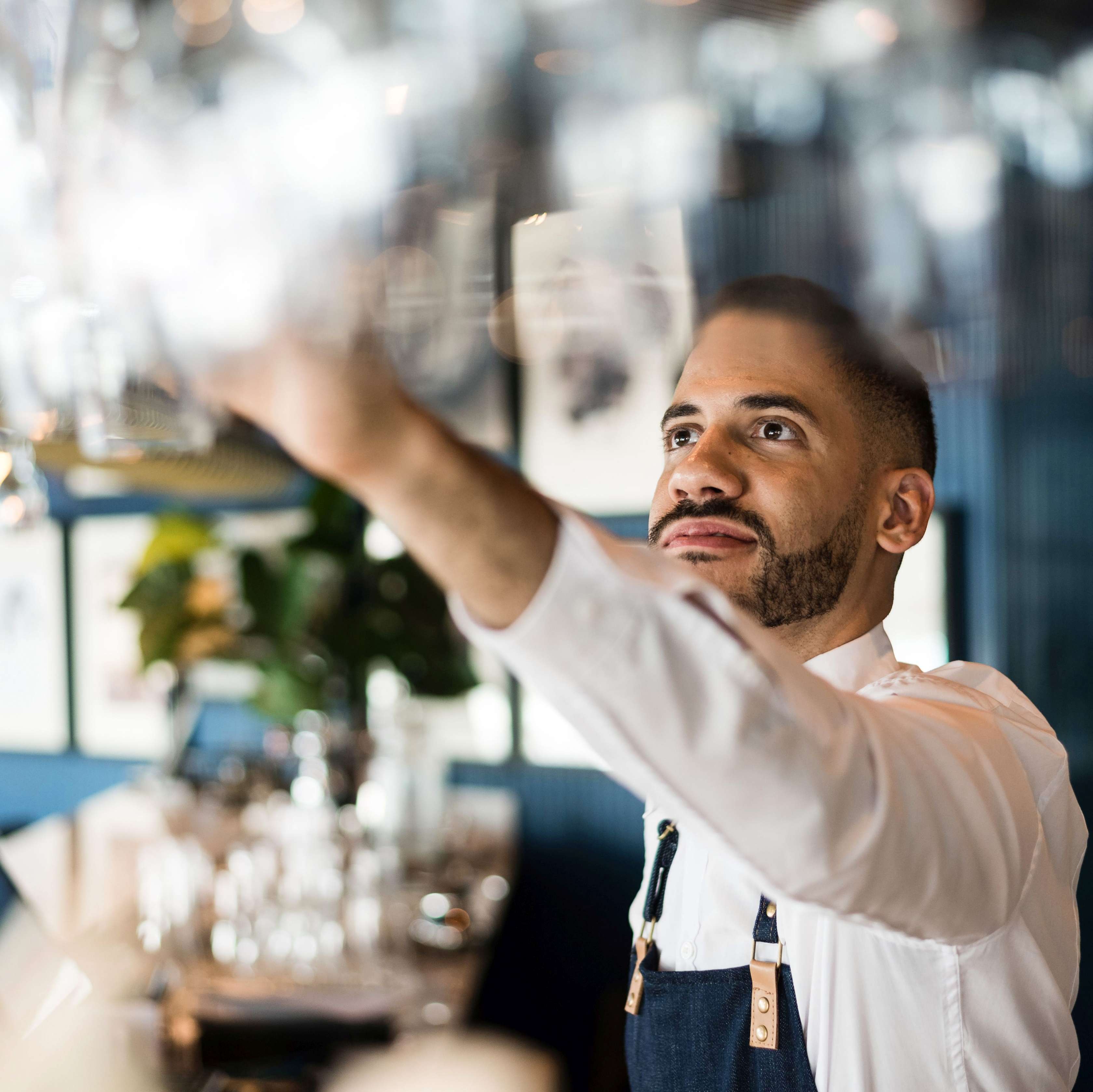 Ein Barkeeper greift hinter seiner Bar nach einem Glas.