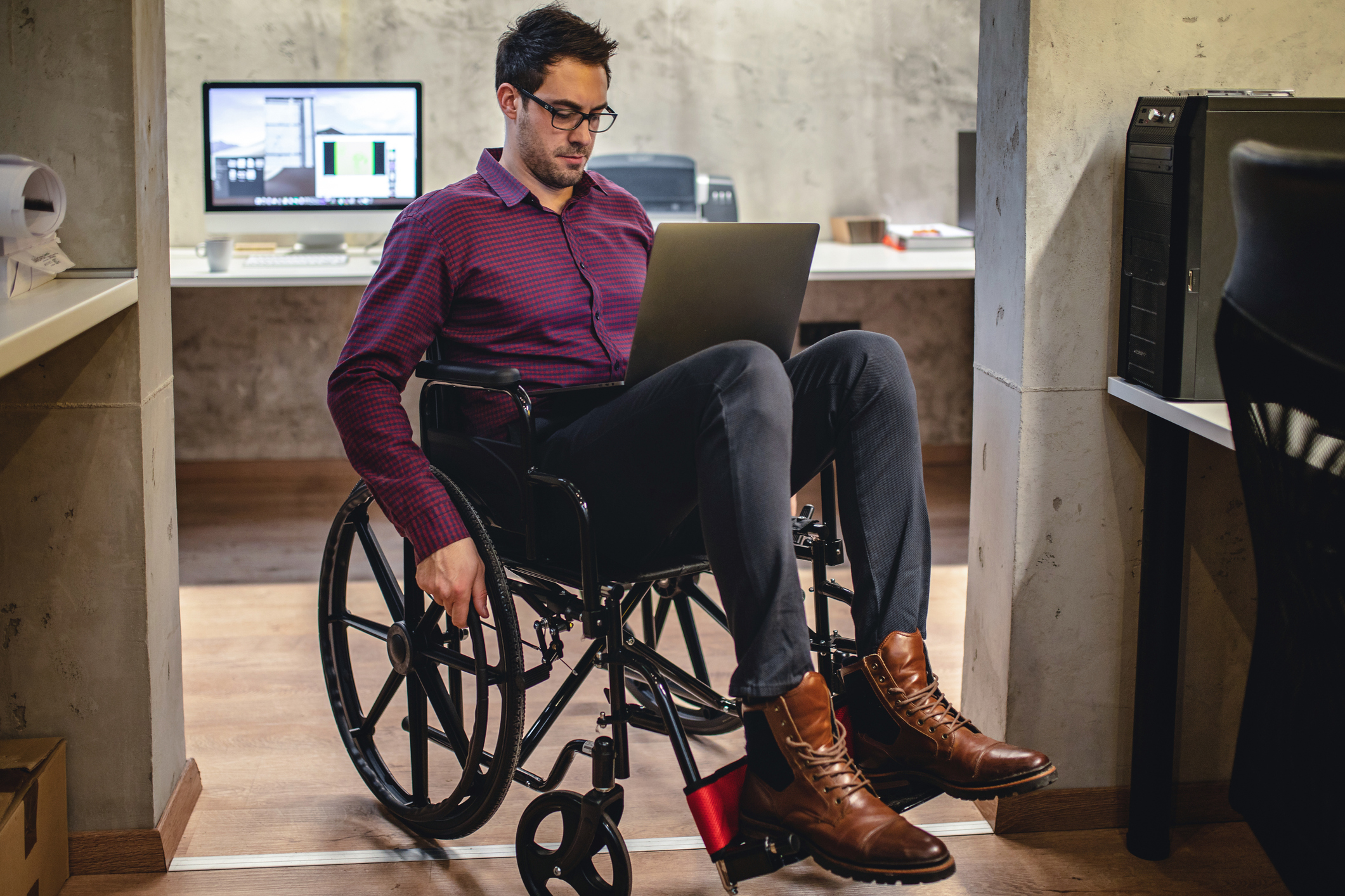 Ein Mann sitzt in einem Rollstuhl und blickt in einen Laptop, der auf seinen Oberschenkeln steht.