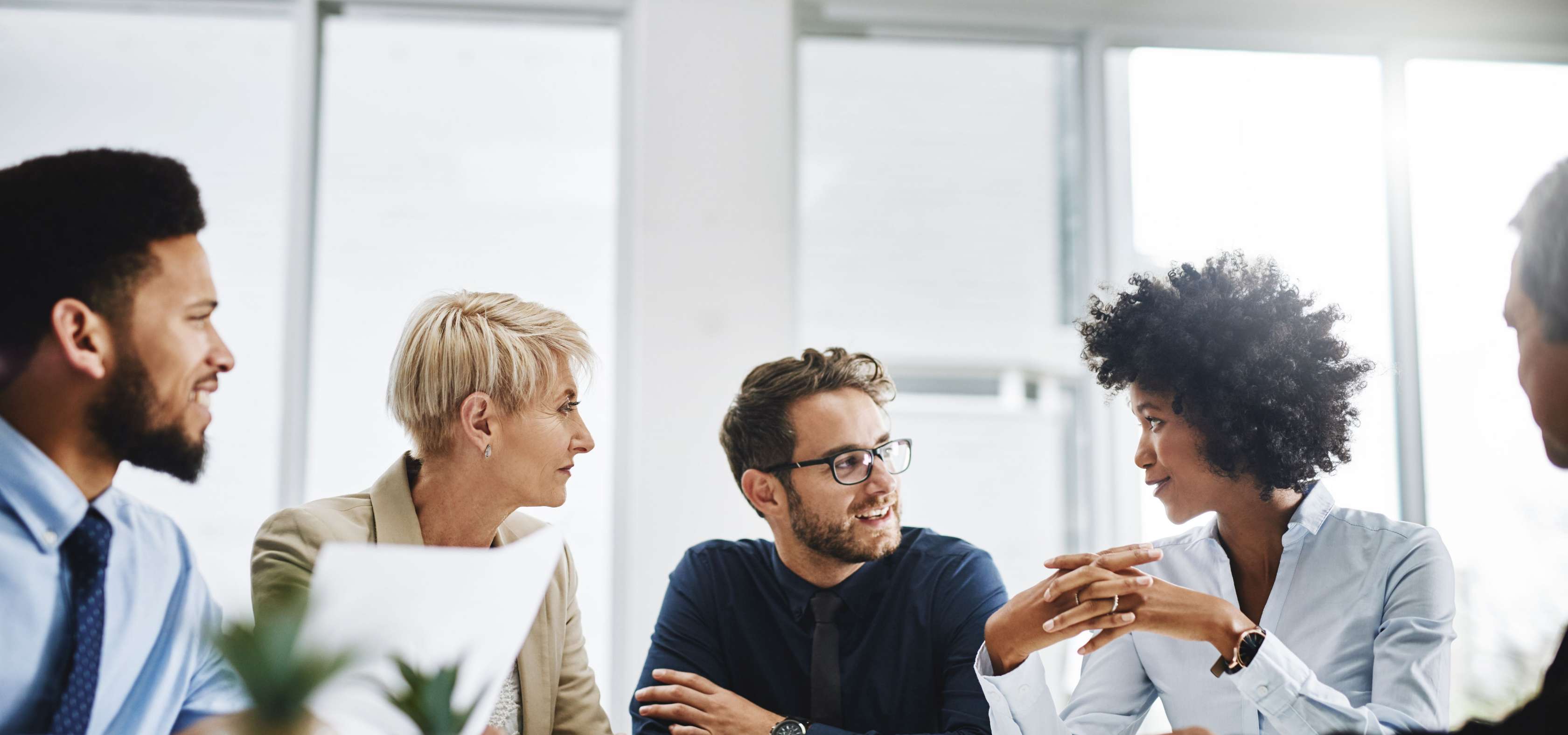 Allianz - Eigene Firma gründen: Vier Personen sitzen in einem Besprechungsraum und sprechen miteinander. Die Gruppe besteht aus zwei Männern und zwei Frauen, die sich freundlich und konzentriert ansehen.