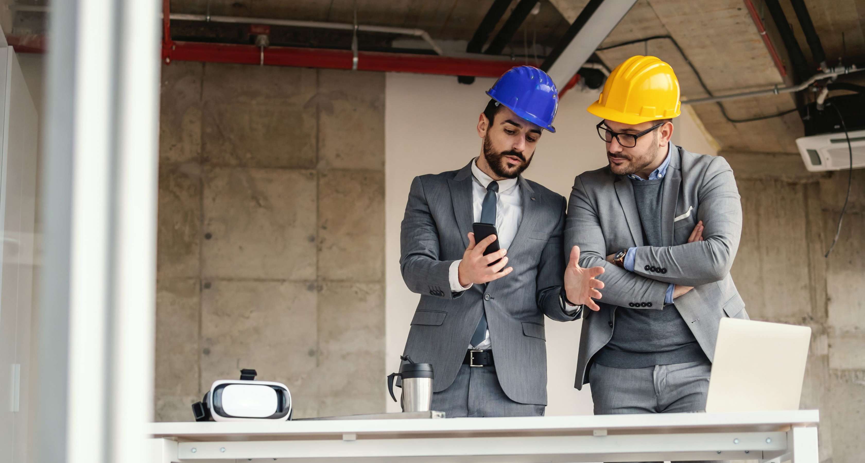 Allianz - Wasserschäden in Gewerberäumen: Zwei Männer mit Bauhelmen stehen in einem Bürogebäude vor unverputzten Wänden.
