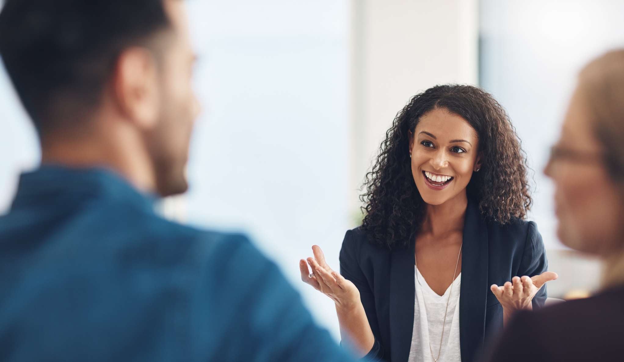 Allianz - Firmenrechtsschutz - Absicherung Ihres Unternehmens: Eine Frau in einem Blazer lächelt und gestikuliert freundlich, während sie mit einer adneren Person spricht. 