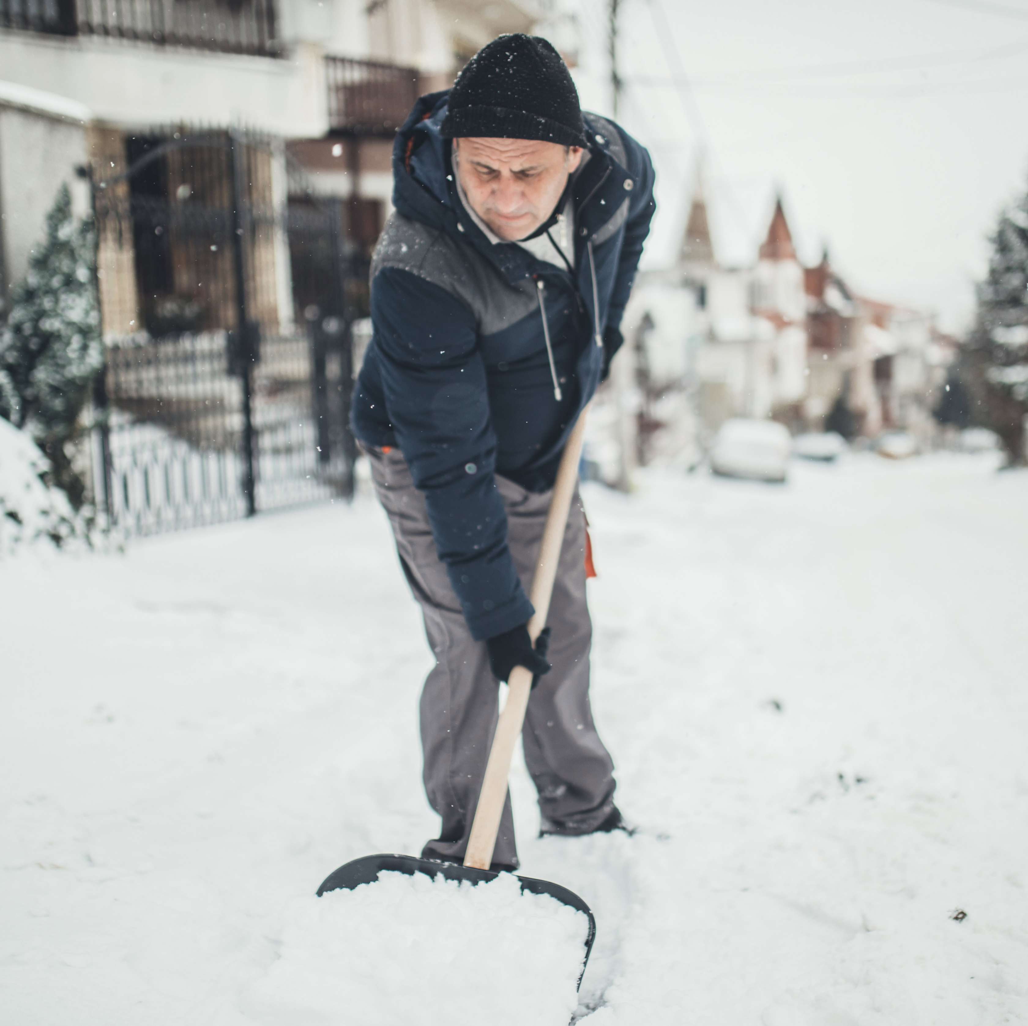 Ein älterer Mann in schwarz-grauer Jacke und Mütze räumt auf einer Winterstraße Schnee