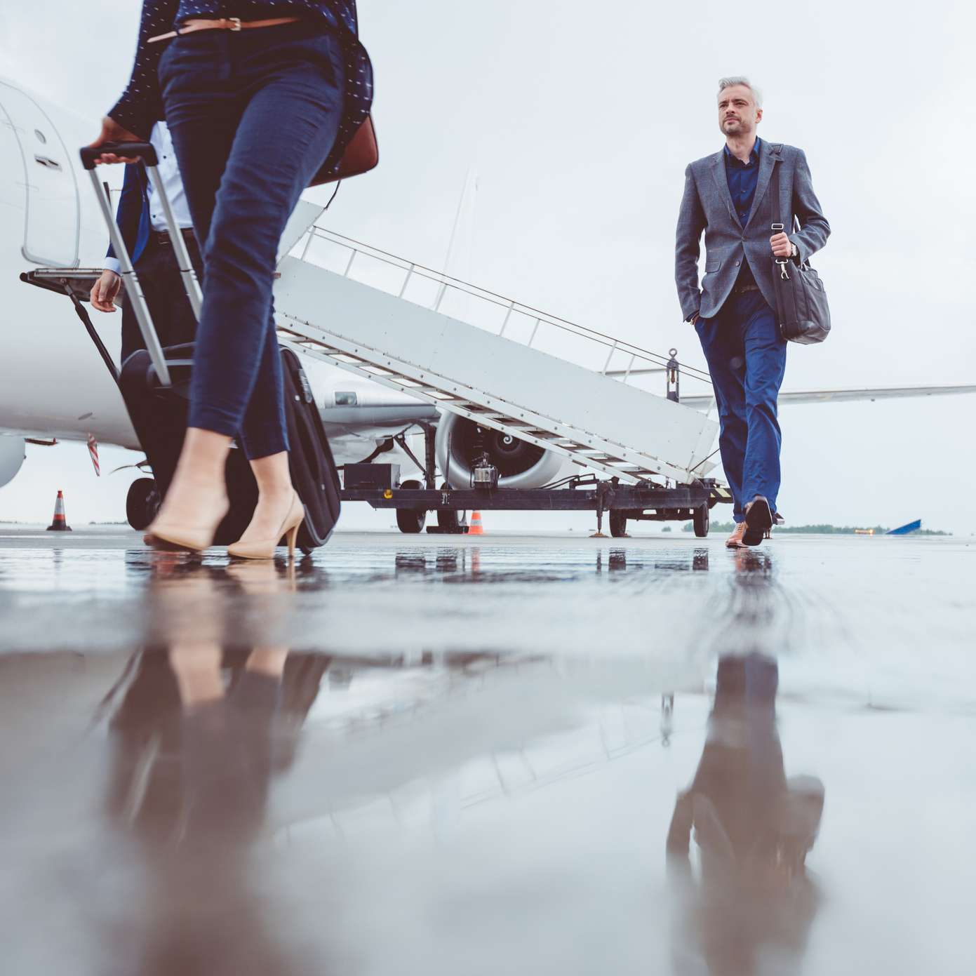 Allianz: Krankenversicherung für Impatriates: Mann und Frau im Business-Kleidung auf Flugfeld vor Flugzeug