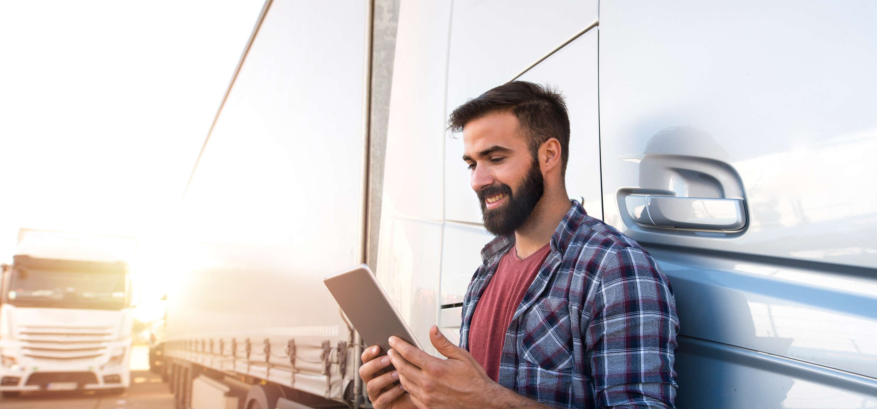 Allianz LKW-Versicherung | Mann steht vor LKW und schaut lächelnd in einen Tablet-Computer.