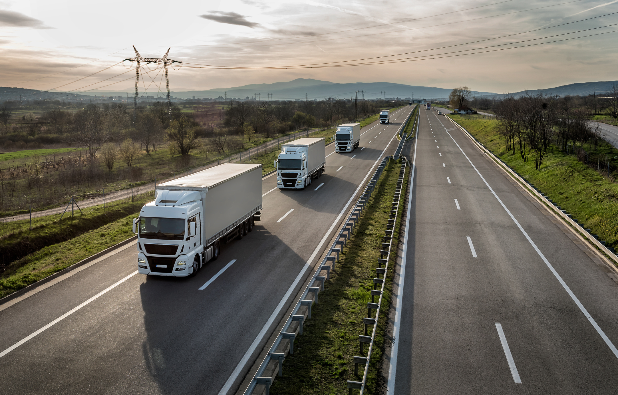 Allianz - Flottenversicherung: Mehrere weiße LKW in einer Reihe auf der Autobahn.