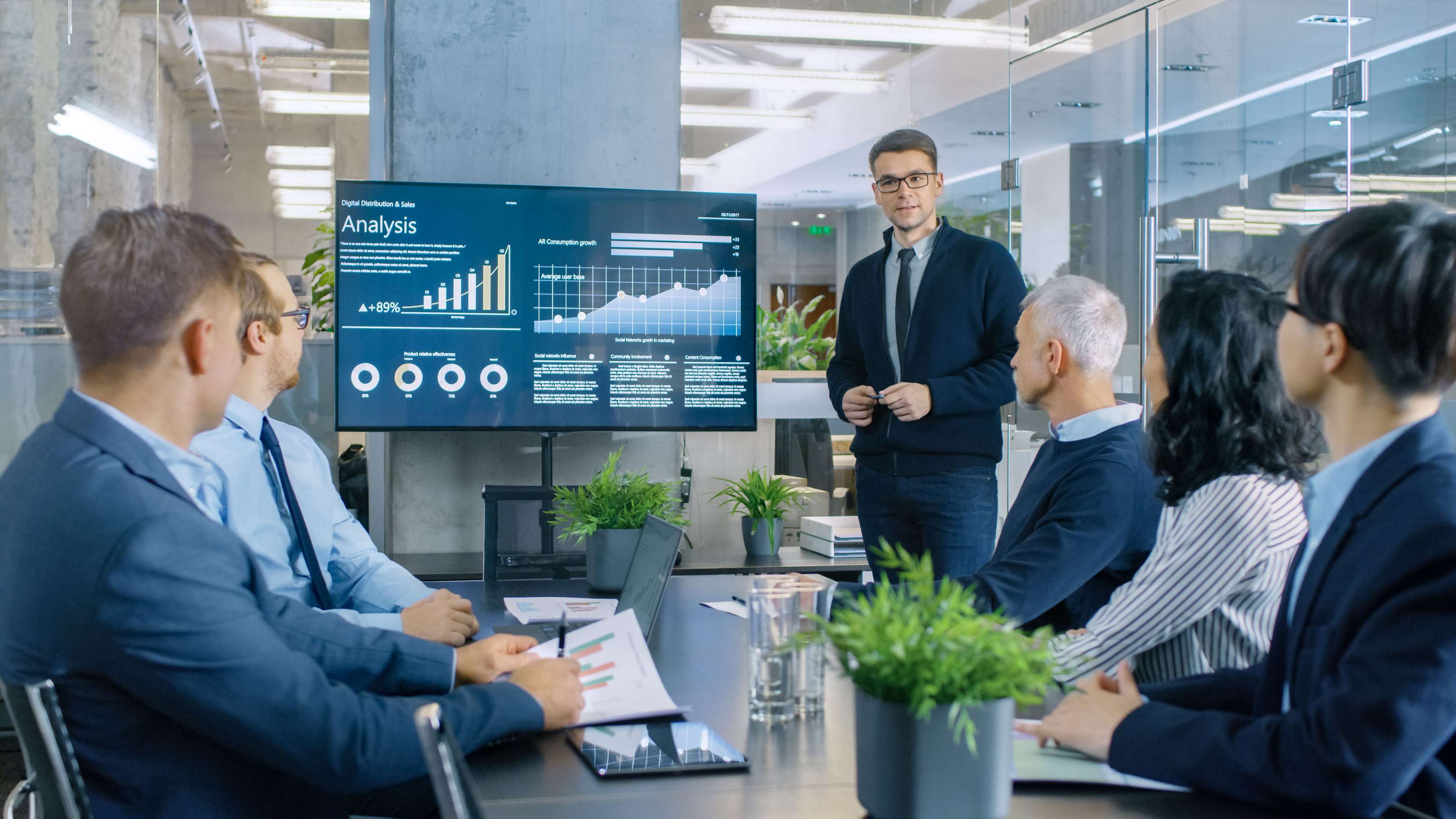 Mitarbeiter eines Unternehmens schauen in einer Besprechung gemeinsam auf einen großen Bildschirm mit Grafiken und Analysen.