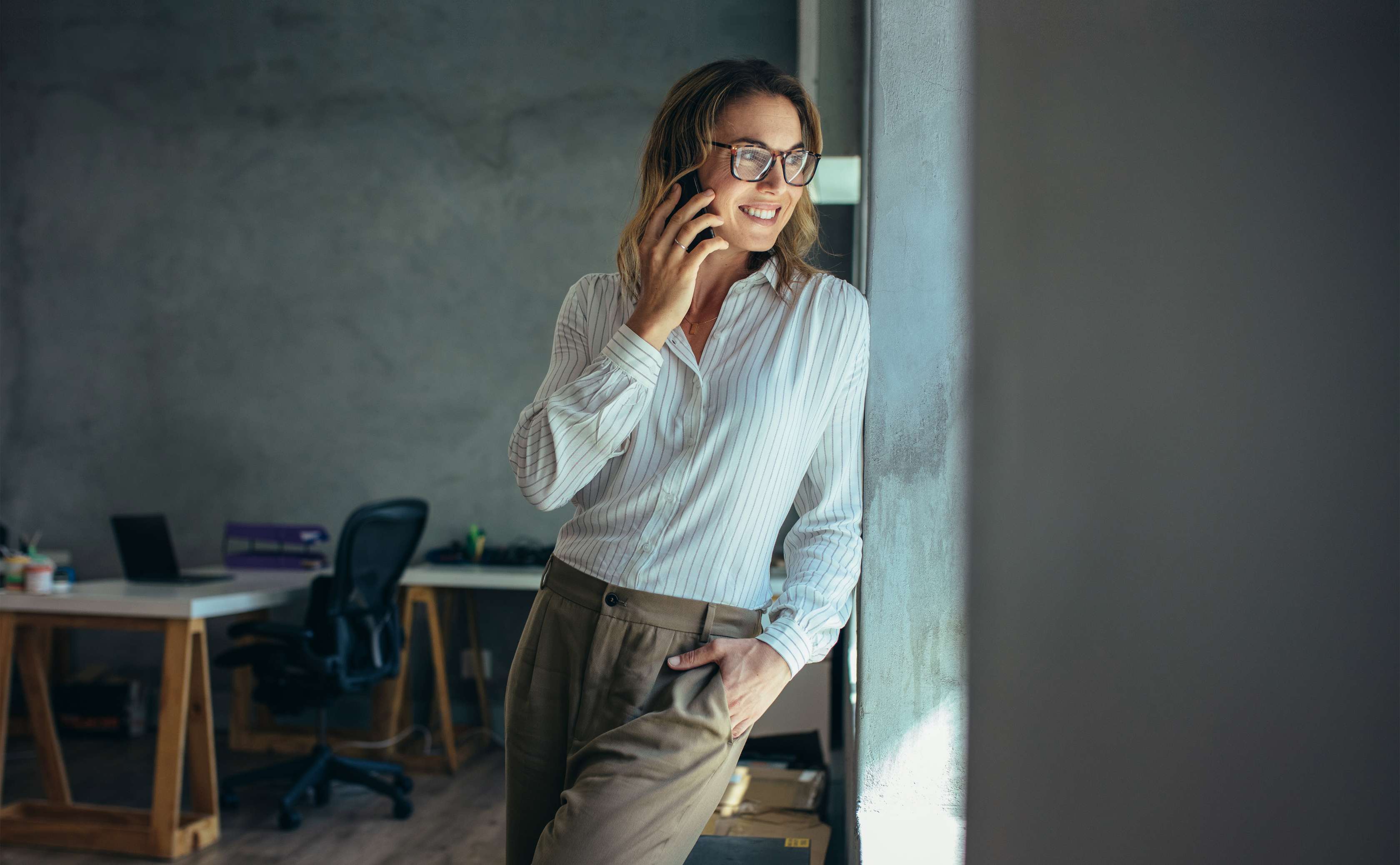 Frau steht telefonierend an die Wand eines Büros gelehnt und schaut dabei aus dem Fenster