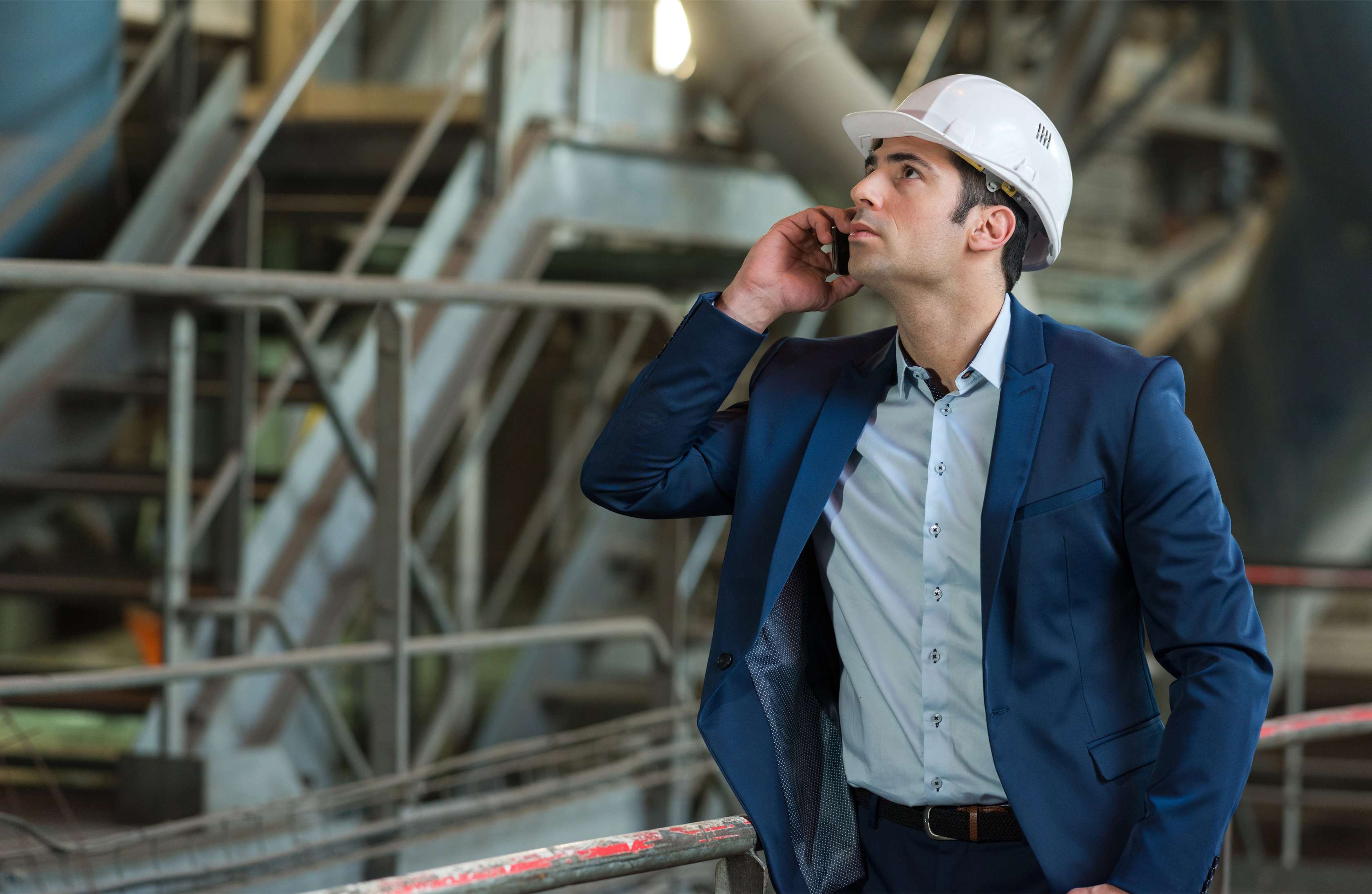 Ein Ingenieur im blauen Anzug und weißem Helm telefoniert und schaut zu einer Pumpe
