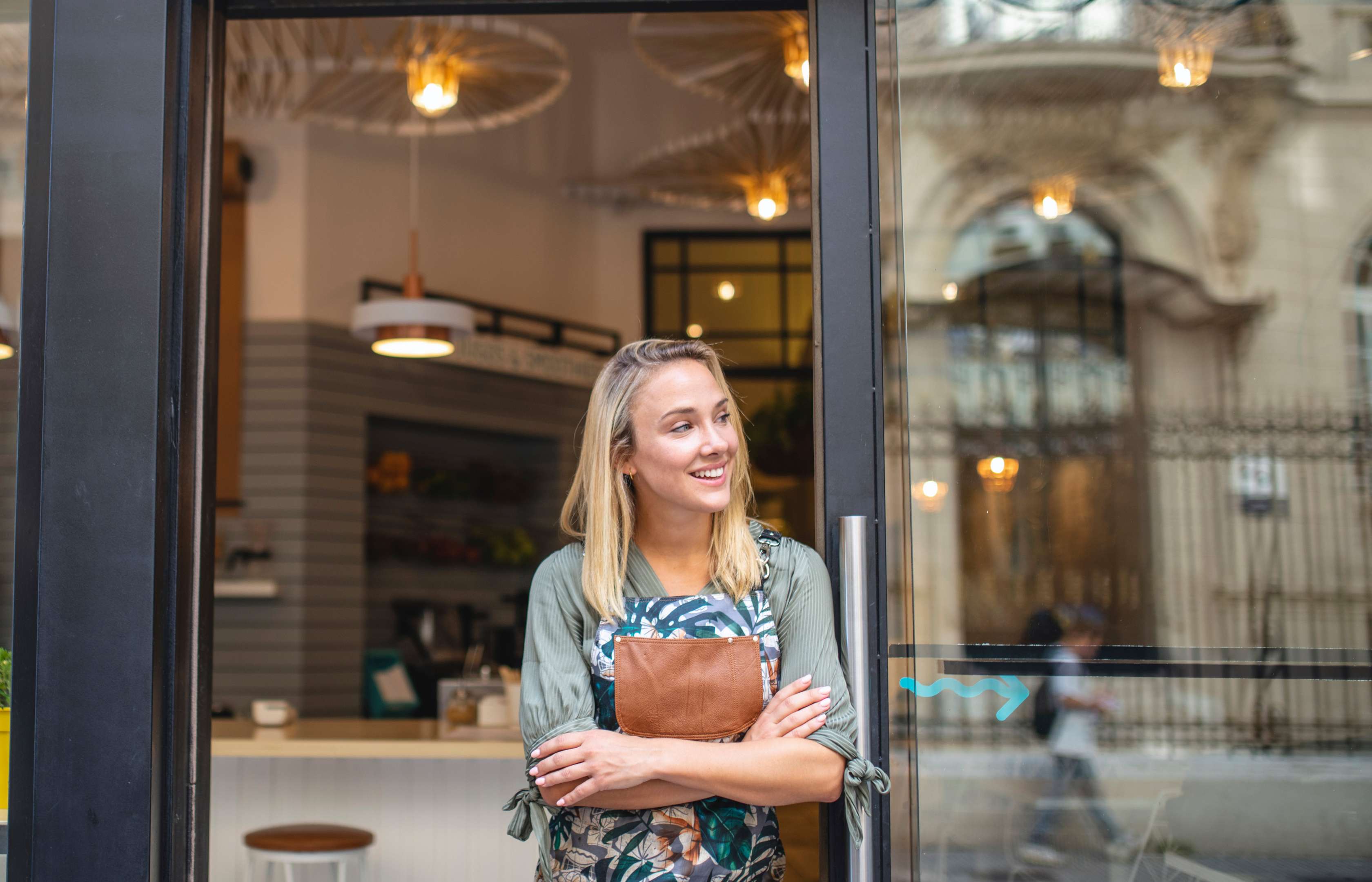 Junge Frau mit Schürze steht vor einem Coffee Shop