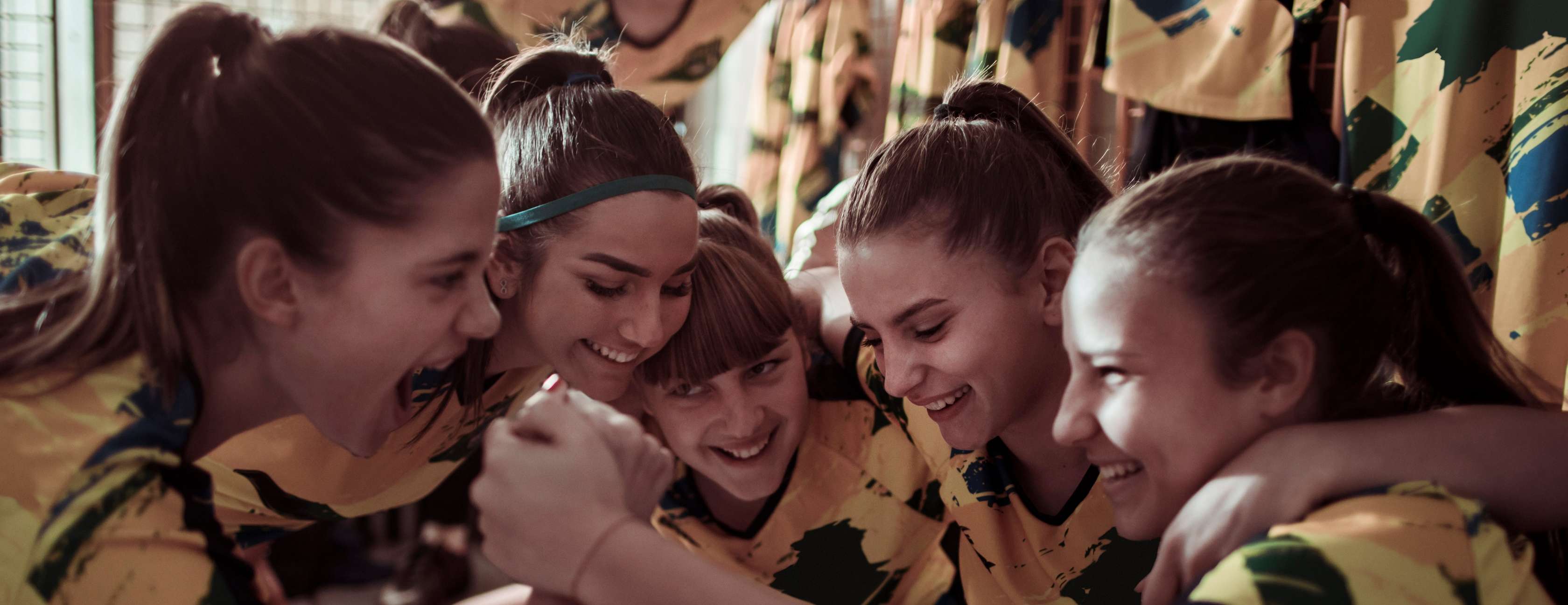 Mädchen einer Sportmannschaft in gelb-grünen Trikots umarmen sich lachend.