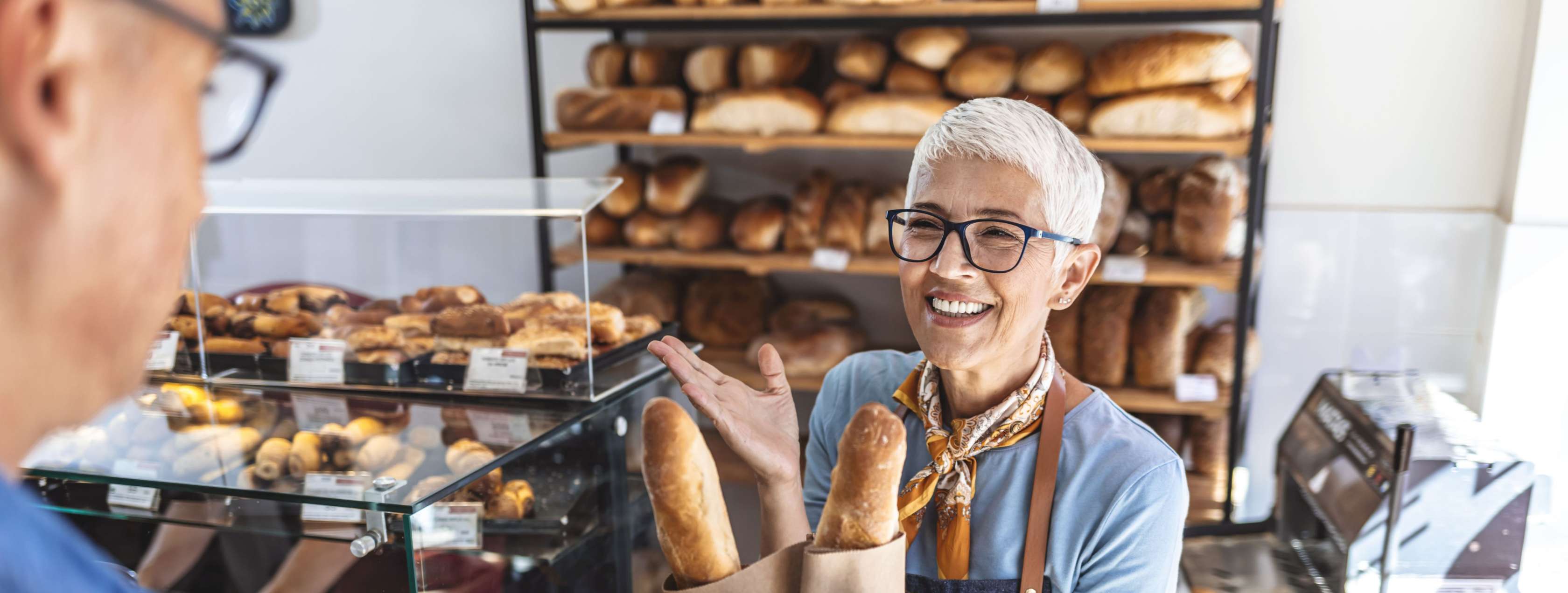 Verkäuferin steht mit Broten in der Hand hinter dem Tresen eines Ladens