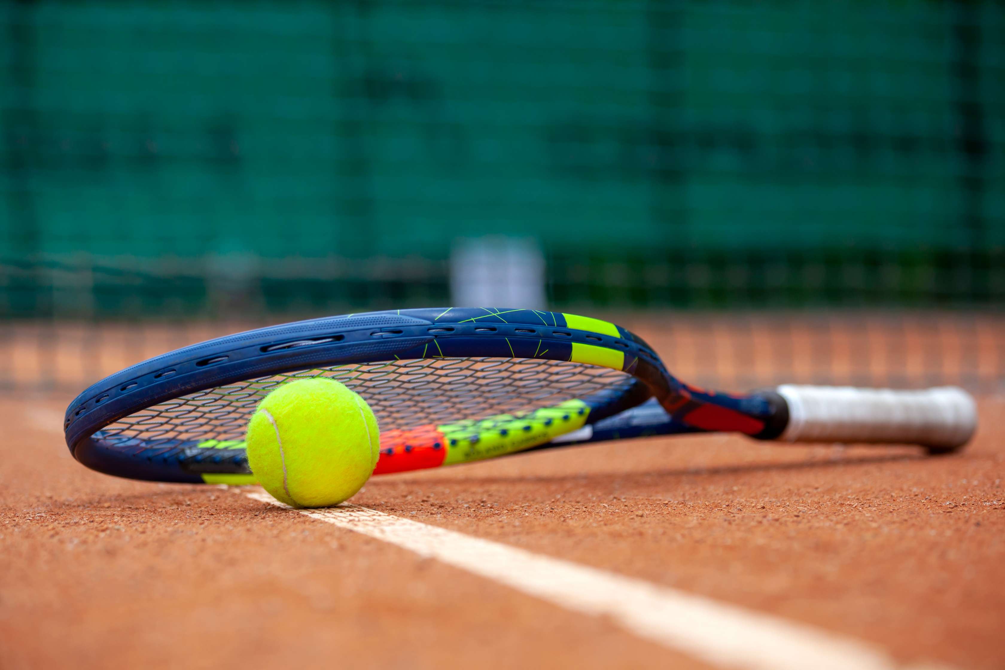 Ein Tennisschläger liegt auf einem Tennisball auf dem Spielfeld.