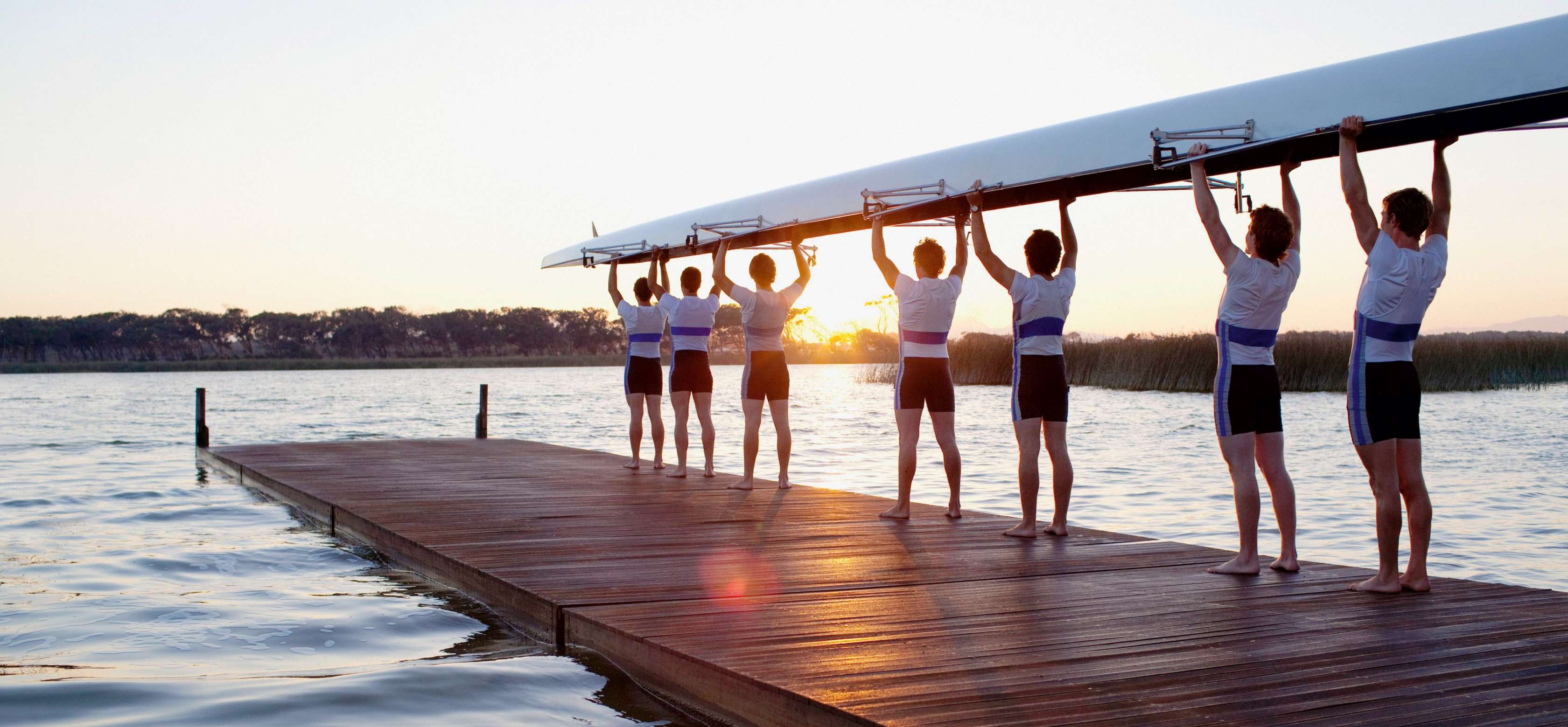 Vereinsversicherung - Gruppe von Ruderern steht mit Boot auf einem Steg am Wasser