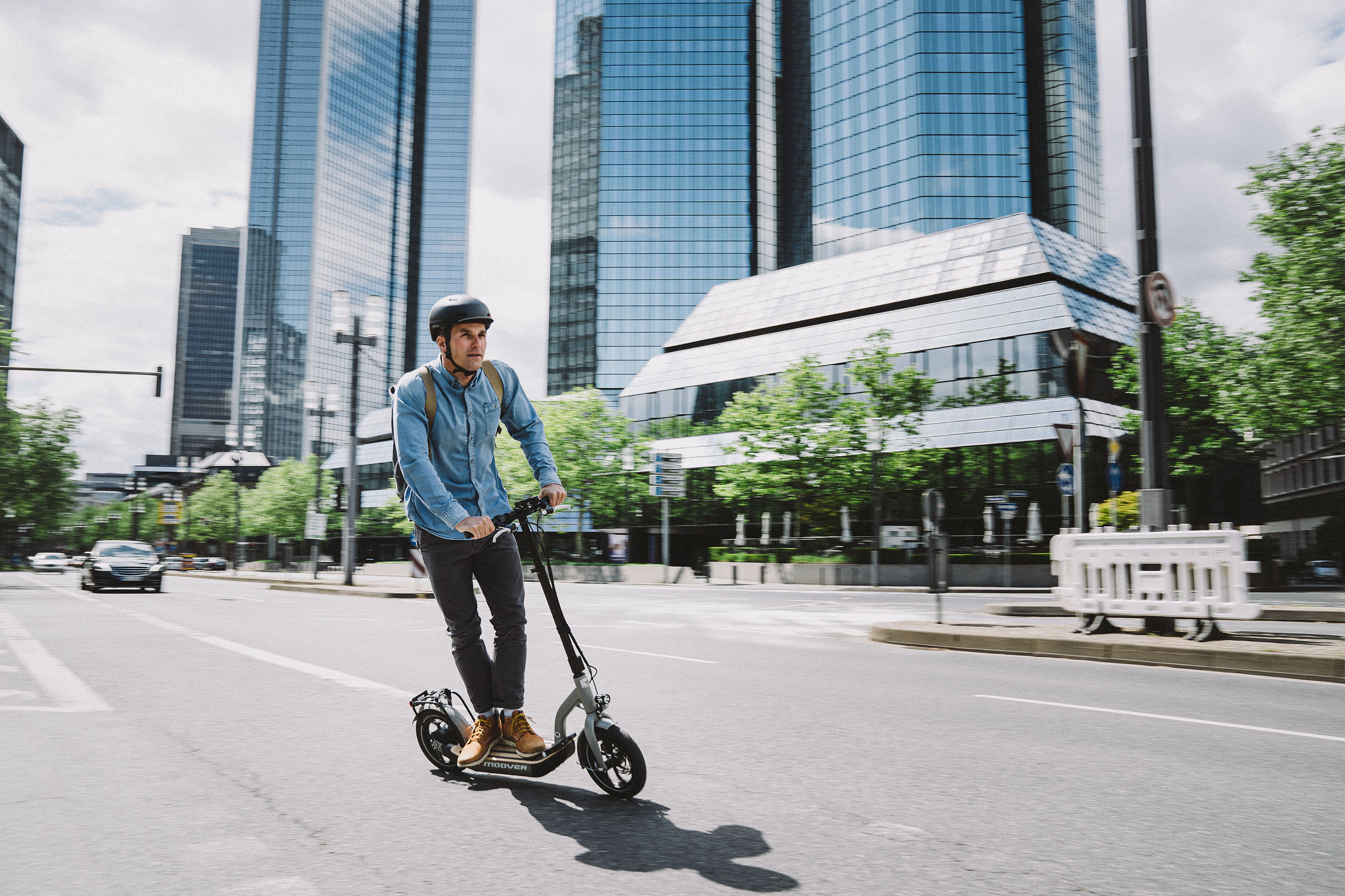 Junger Mann mit Helm fährt mit E-Scooter auf Straße durch Großstadt