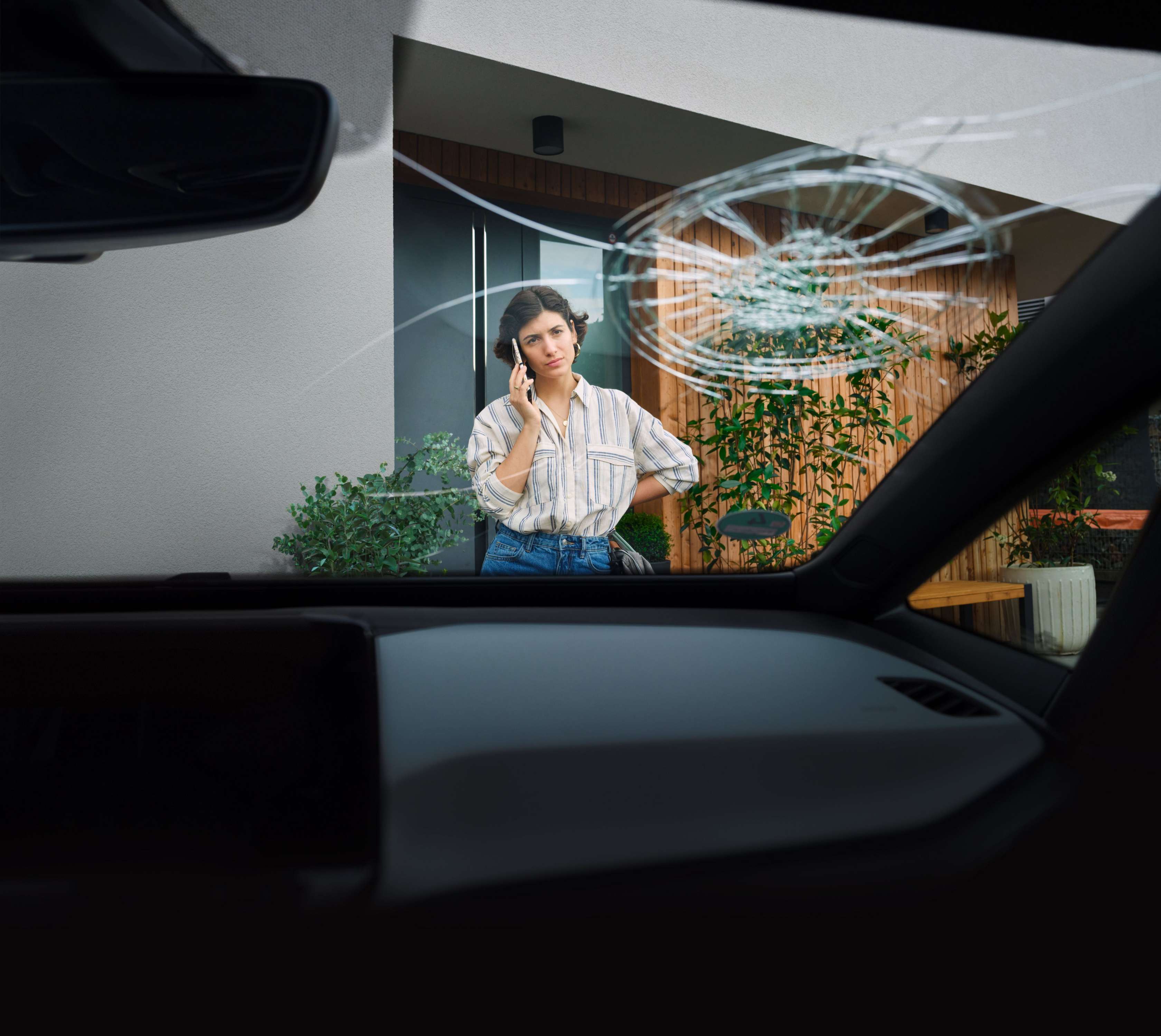 Kfz-Versicherung: Frau steht telefonierend vor Auto mit gesprungener Windschutzscheibe.