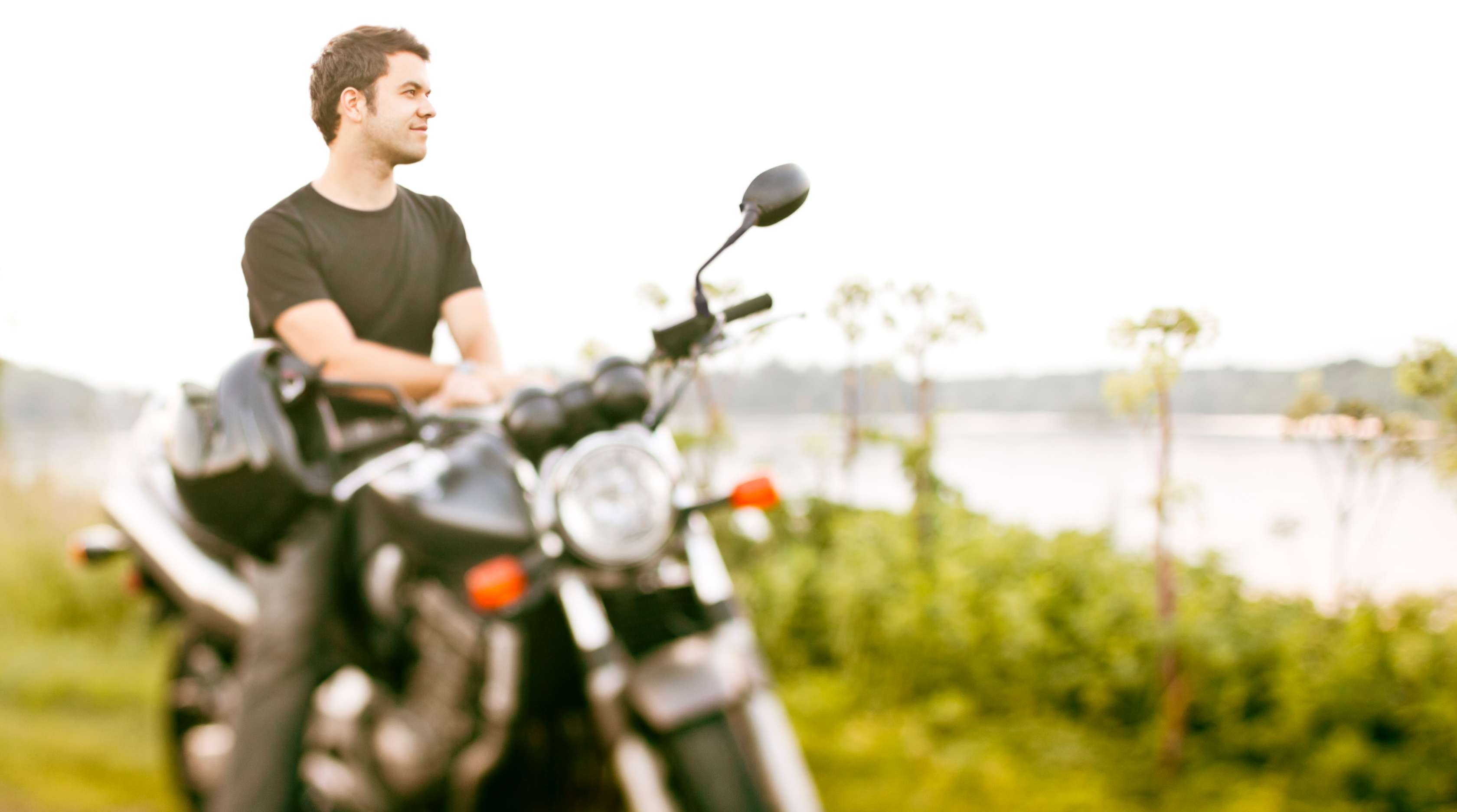Allianz - Mann auf Motorrad blickt auf einen See