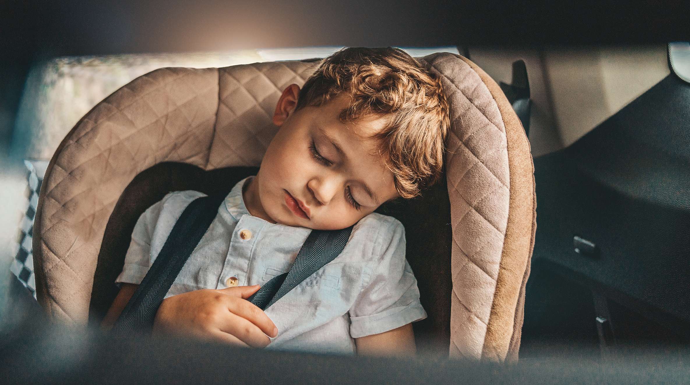 Allianz - Vollkaskoversicherung: Kleiner Junge schläft beruhigt im Kindersitz auf der Rückbank eines Autos