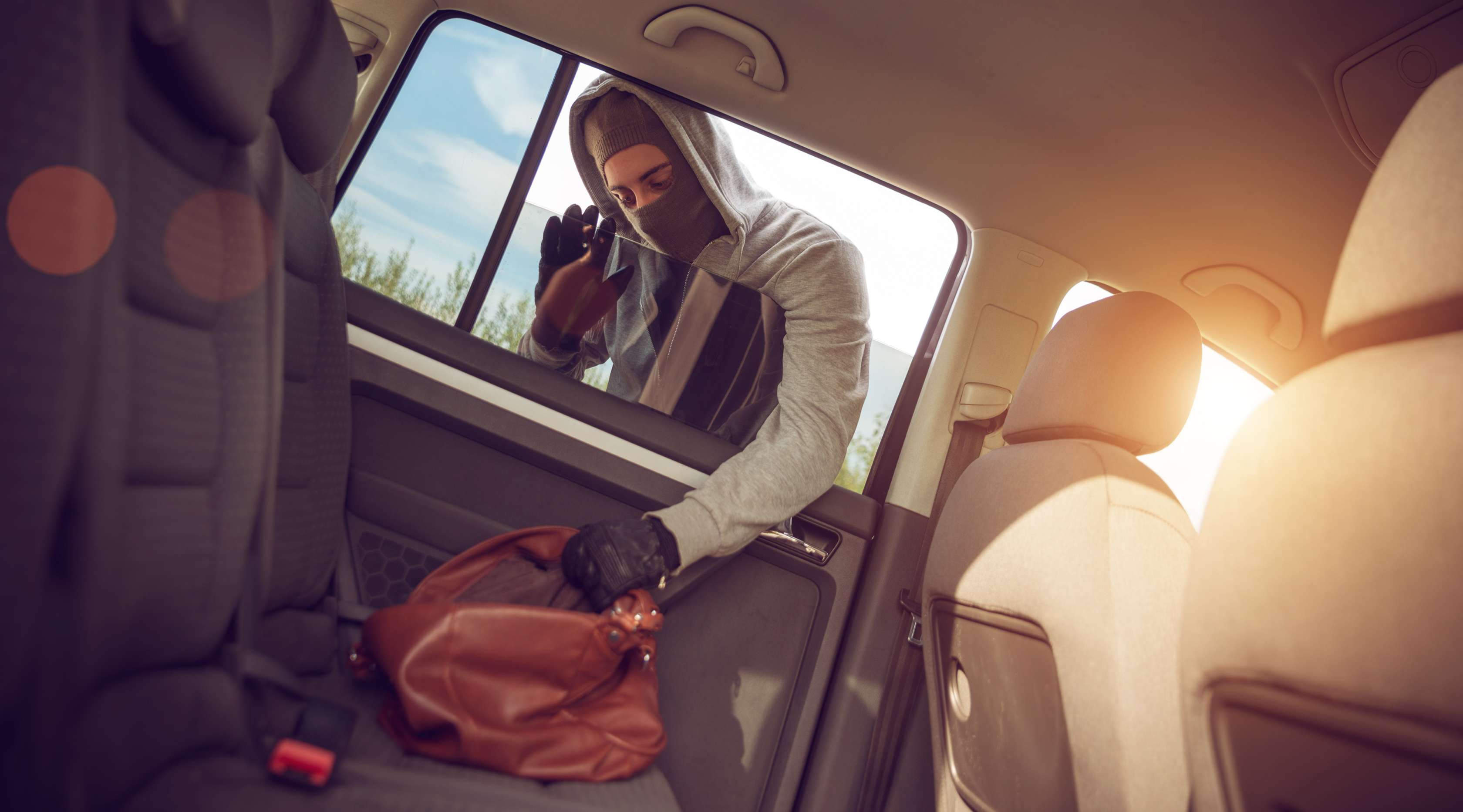 Allianz - Kfz-Versicherung Diebstahl aus Auto: Maskierter Dieb greift durch Seitenfenster eines Pkw eine Handtasche, die auf dem Rücksitz liegt