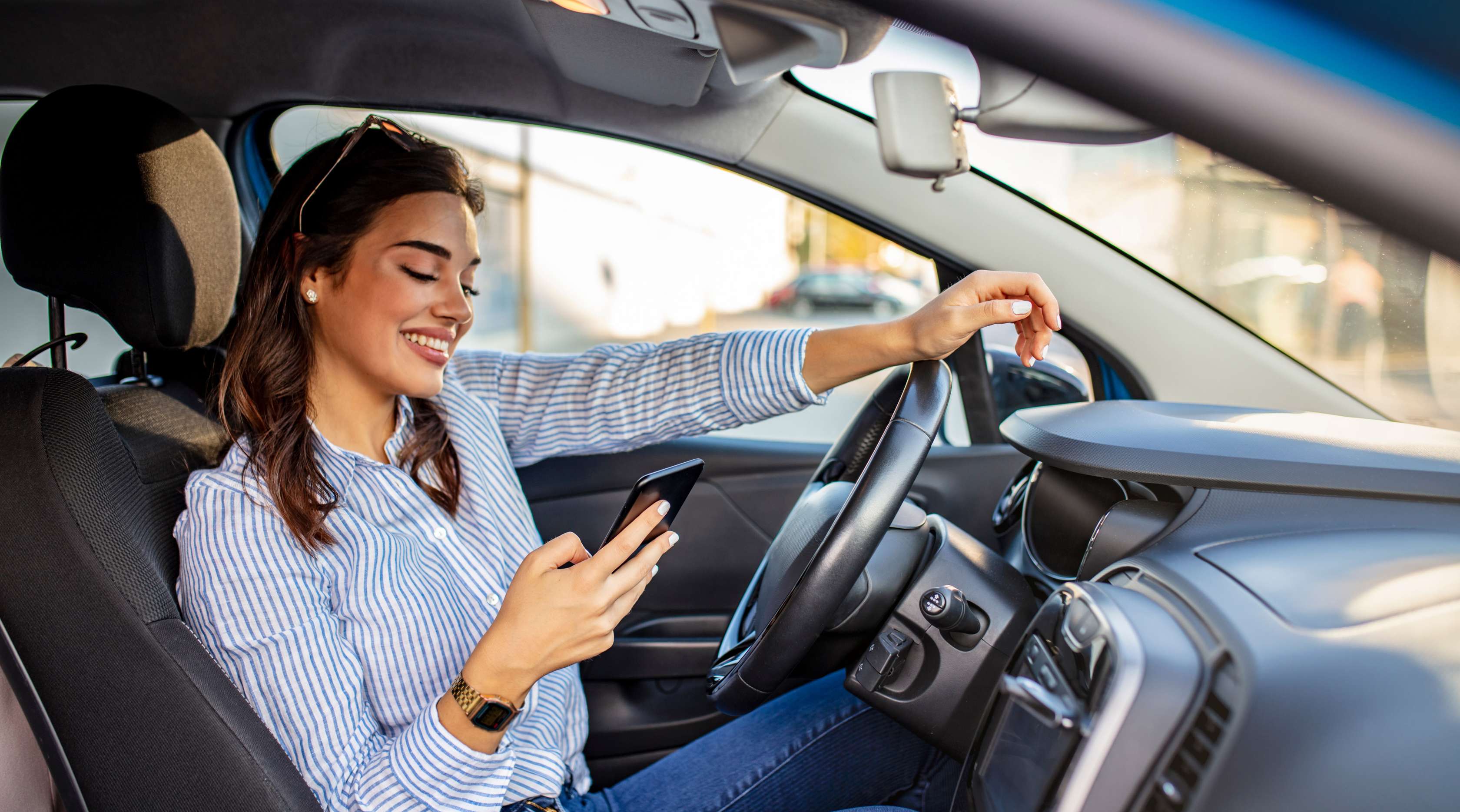 Eine junge Frau sitzt im stehenden Auto und liest auf einem Smartphone