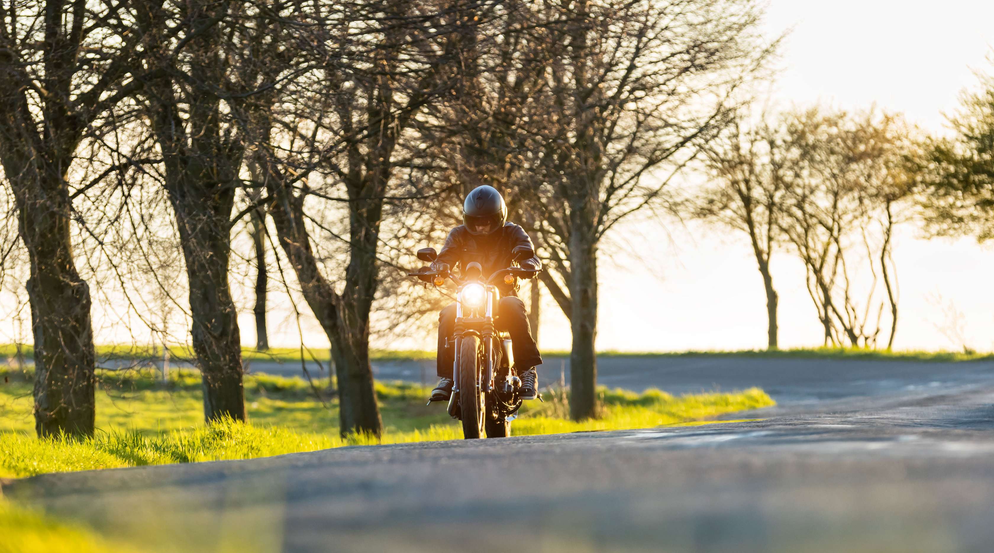 Motorradfahrer mit Helm und schwarzer Schutzbekleidung fährt auf Landstraße