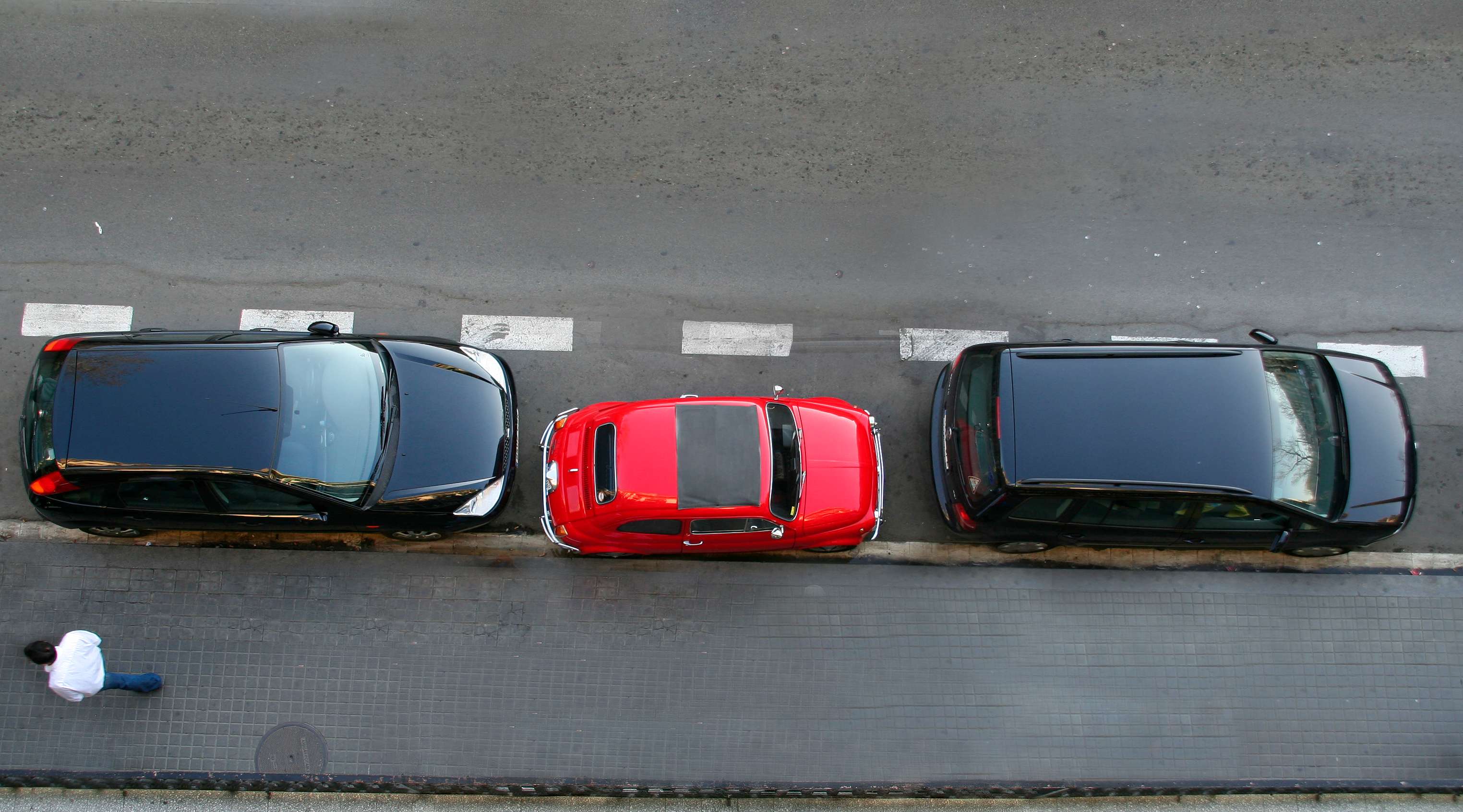 Kleines rotes Auto steht zwischen zwei großen schwarzen Pkw