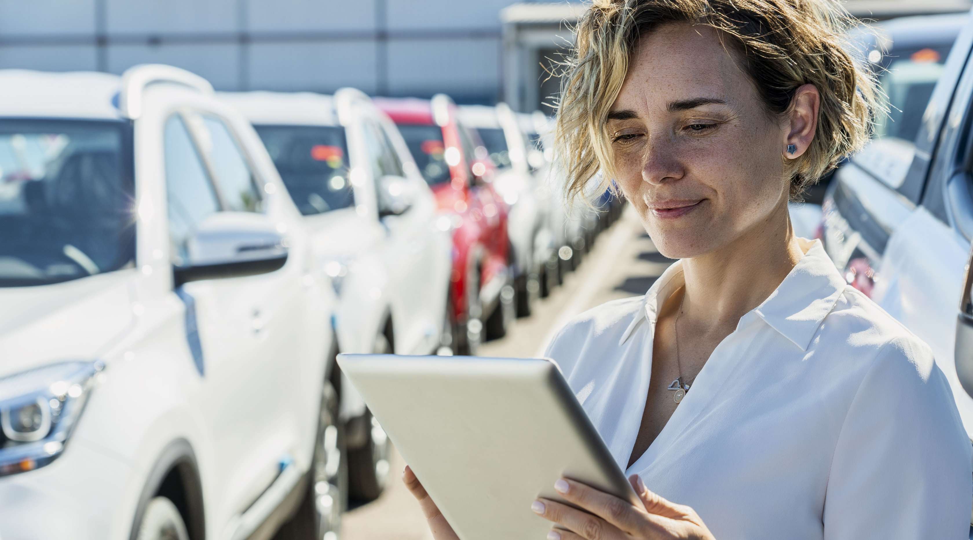 Allianz - Flottenversicherung: Eine Geschäftsfrau steht mit einem Ipad zwischen mehreren Geschäftswagen.
