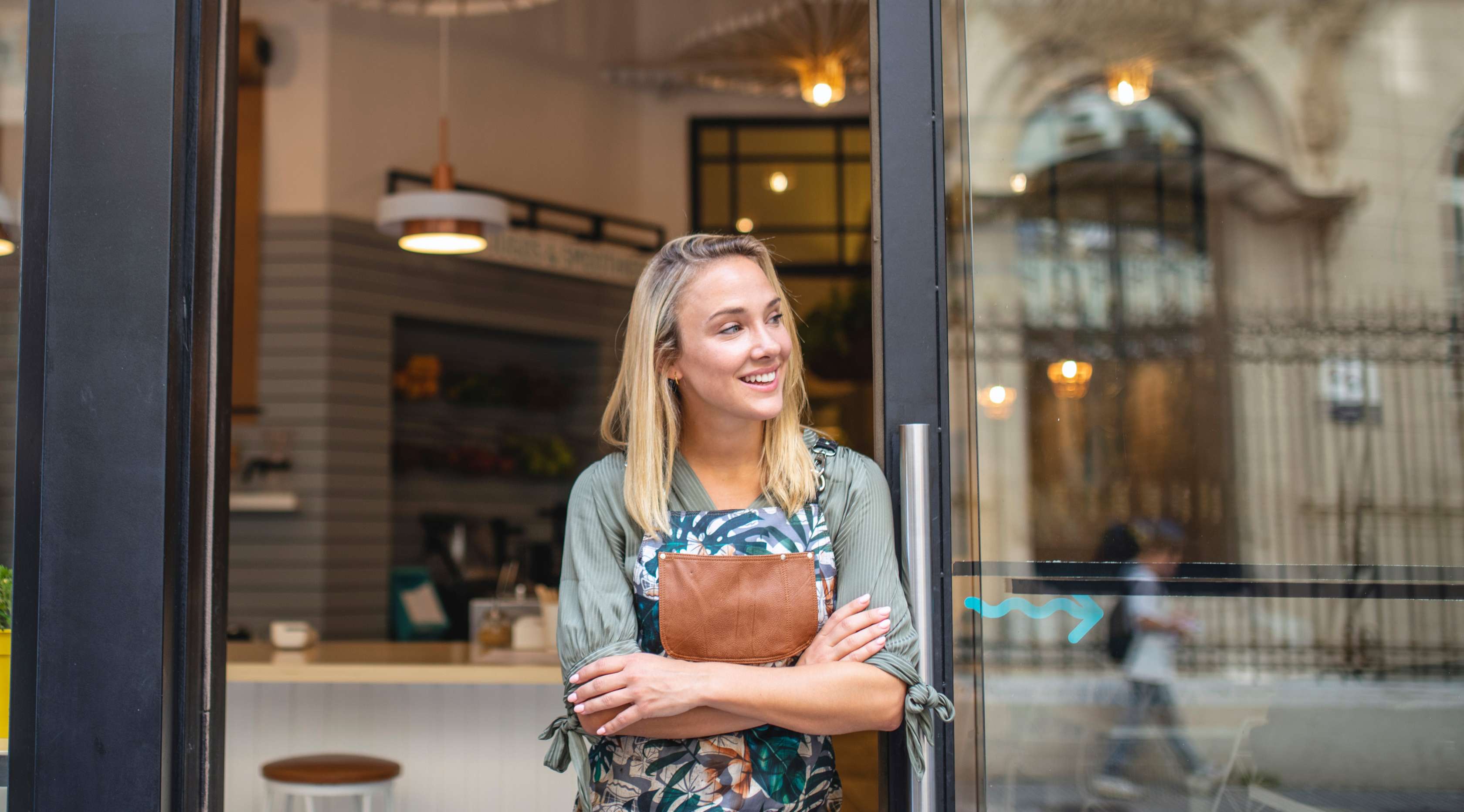 Junge Frau mit Schürze steht vor einem Coffe Shop