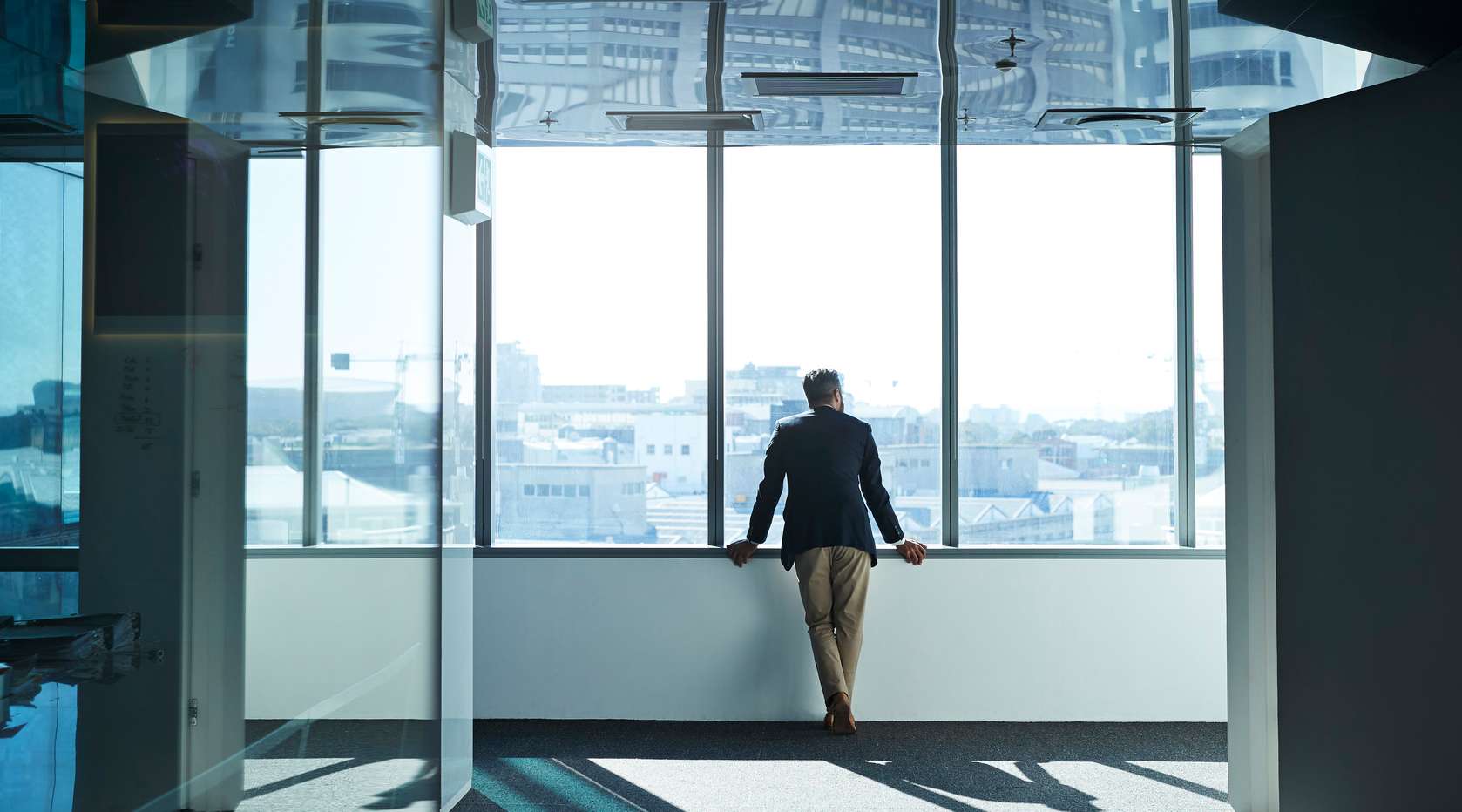 Allianz - Immobilienversicherung für Firmen: Mann steht in einem großen modernen Büro am Fenster und schaut raus