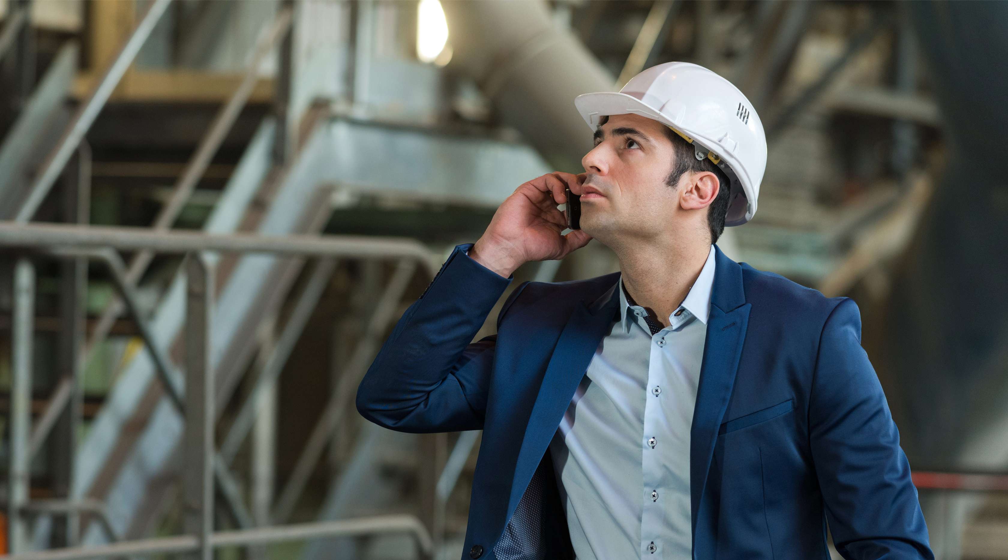 Ein Ingenieur im blauen Anzug und weißem Helm telefoniert und schaut zu einer Pumpe