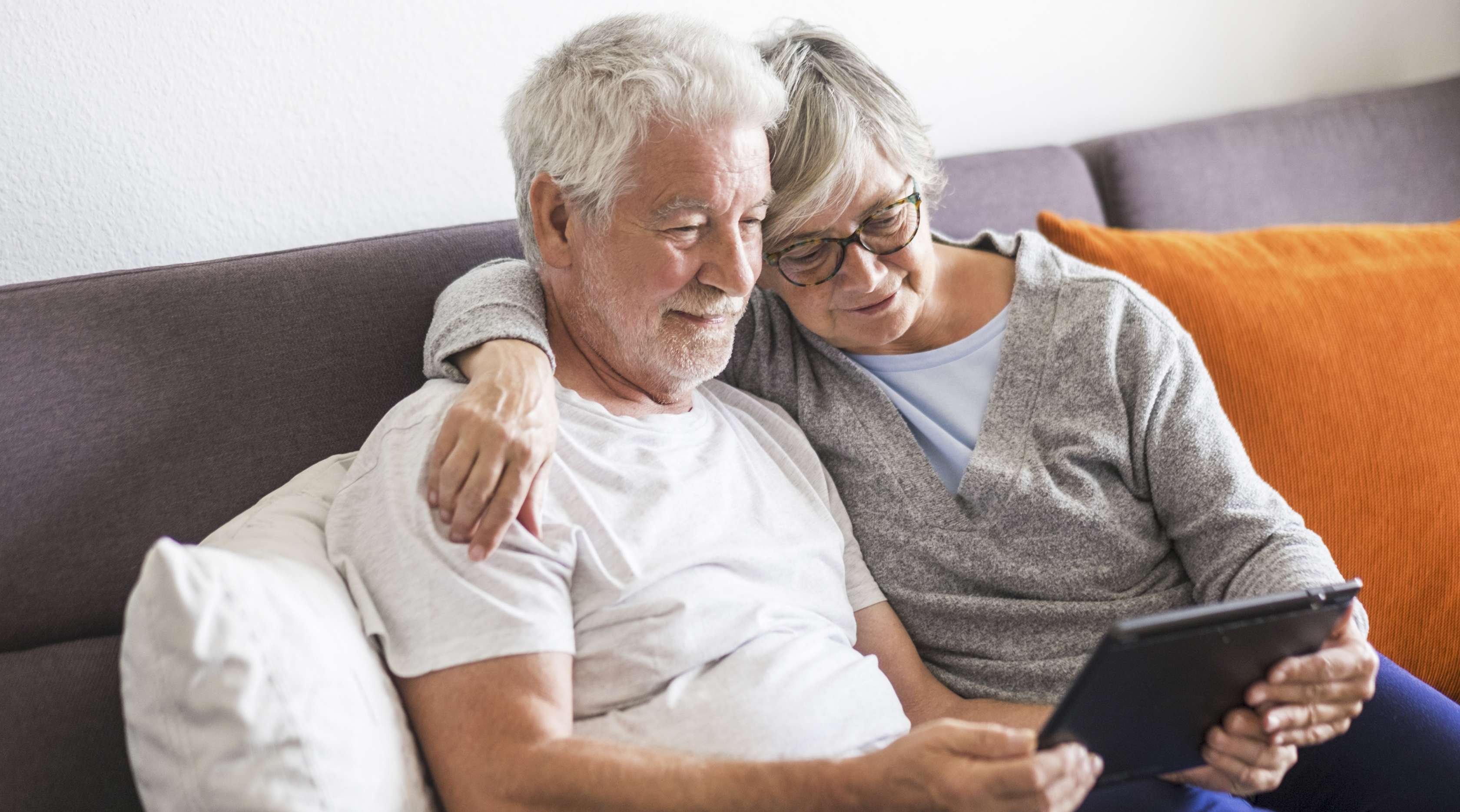 Senioren-Pärchen sitzt gemeinsam auf der Couch und schaut auf ein Tablet