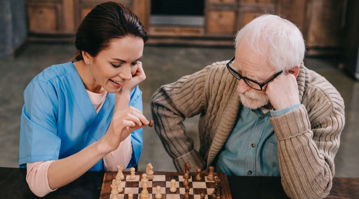 Senior und Pflegerin spielen zusammen Schach