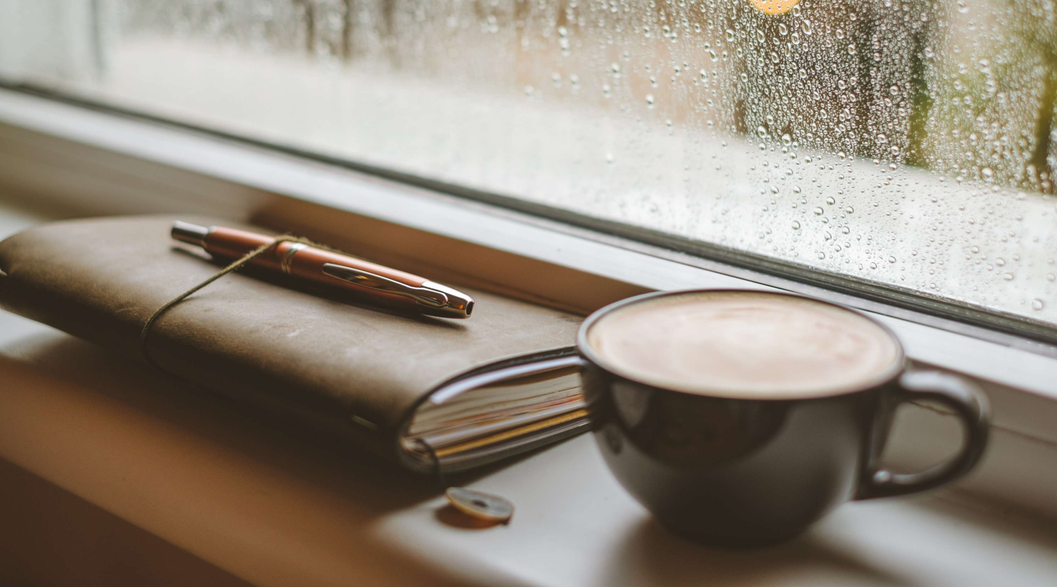 Kaffee und ledernes Notizbuch auf einer Fensterbank