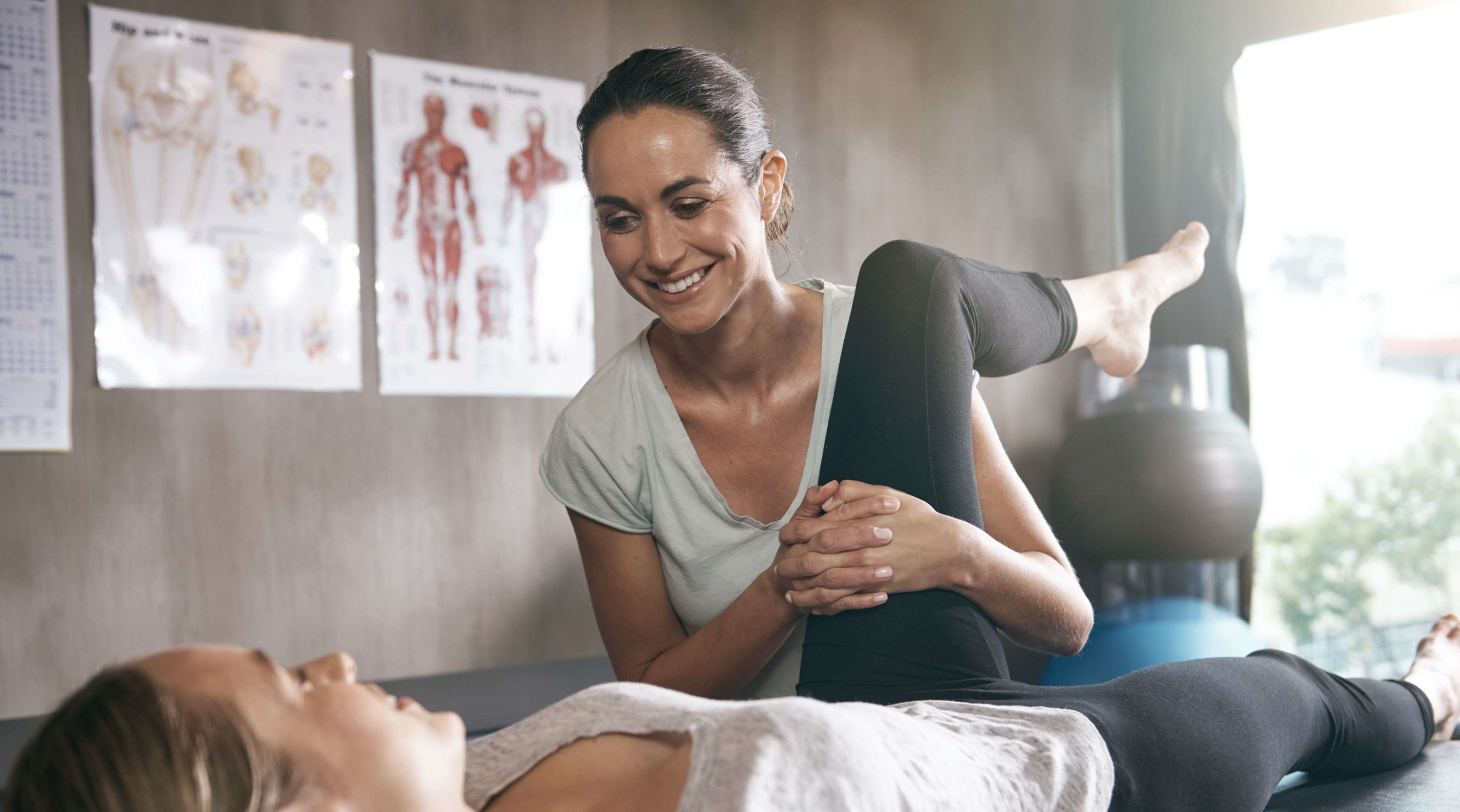 Physiotherapeutin behandelt Patientin, indem sie das Bein Richtung Körper drückt.