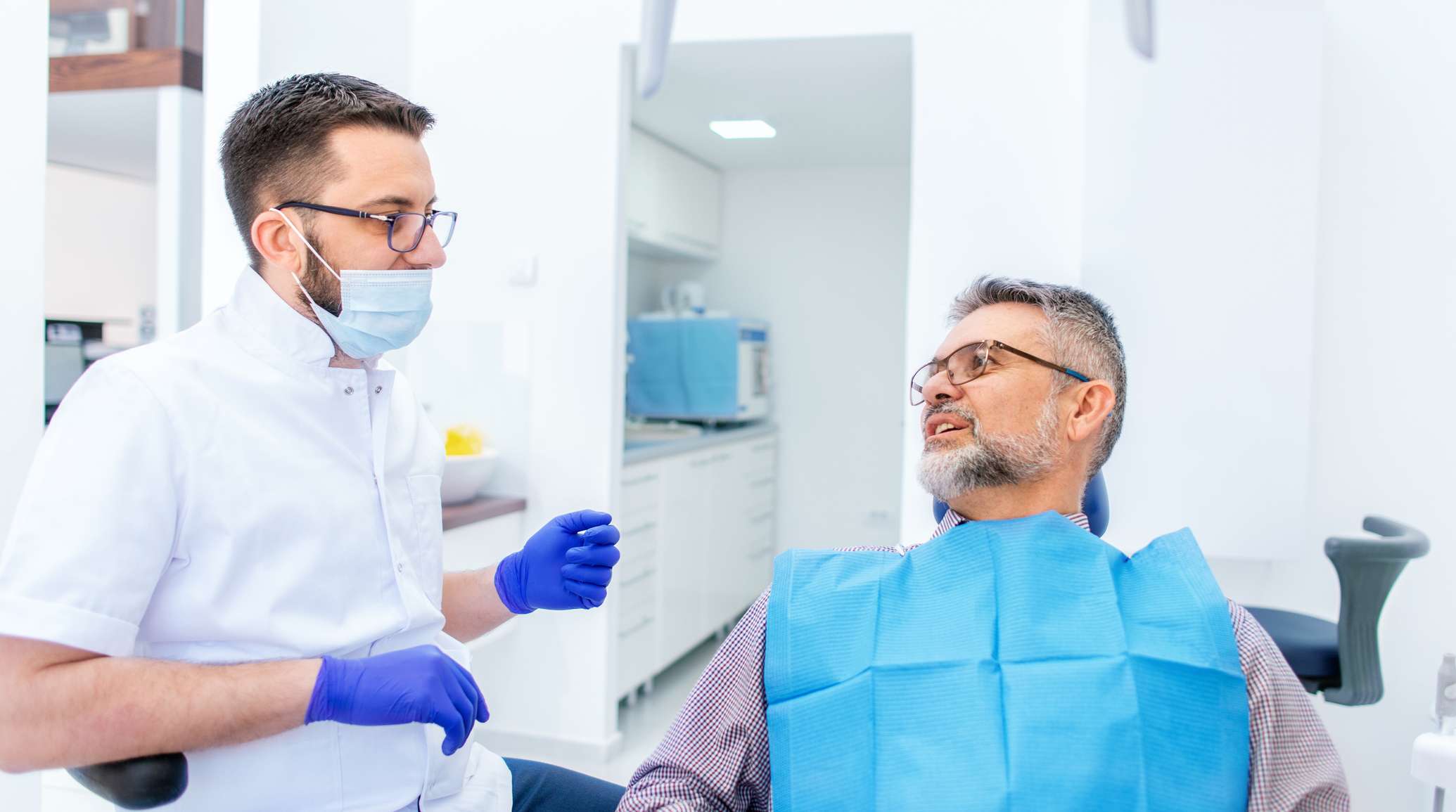 Patient sitzt auf dem Zahnarztstuhl, der Zahnarzt sitzt daneben und bespricht etwas mit dem Patienten.